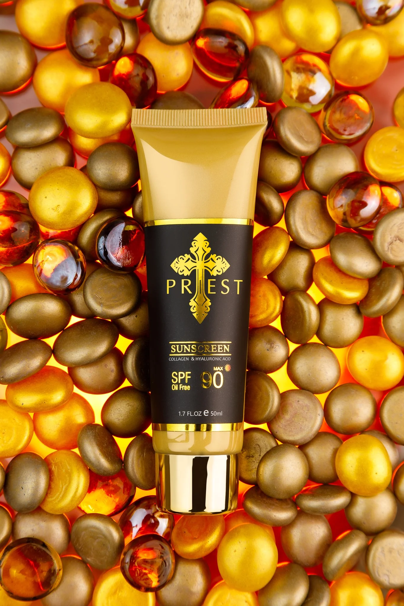 A tube of Priest SPF 90 sunscreen with collagen and hyaluronic acid, placed on a bed of gold and bronze decorative stones.