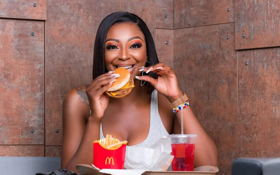 A woman with makeup and a bracelet is eating a cheeseburger at a table with McDonald's fries and a red drink.