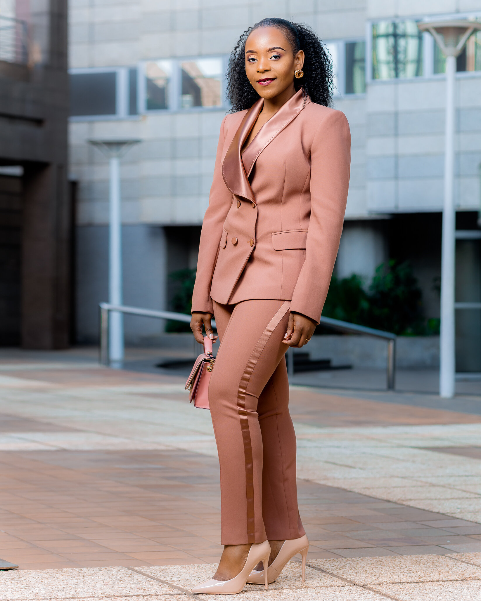 A woman in a pink suit and beige high heels standing outdoors.