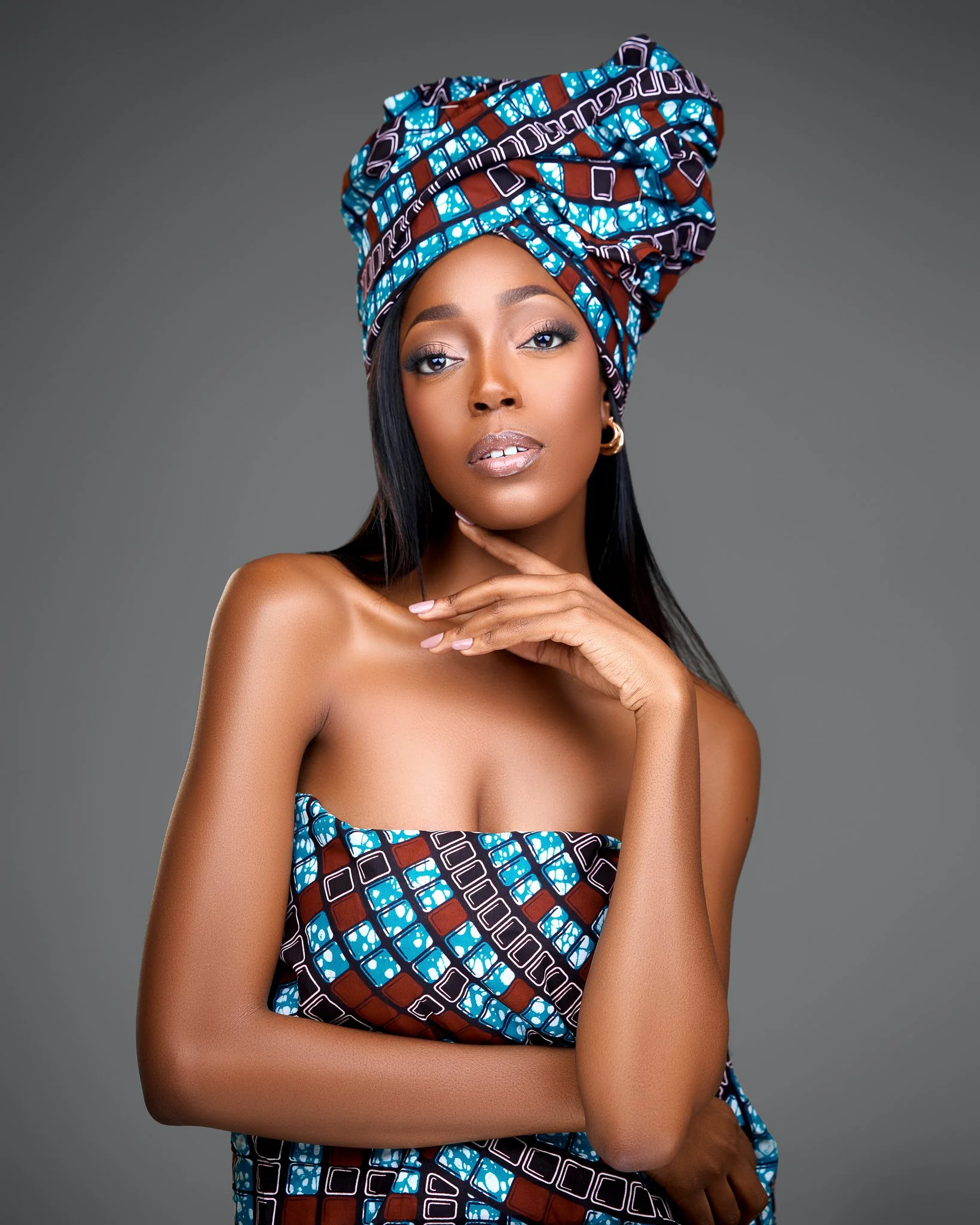 A woman wearing a colorful headwrap and matching strapless dress against a grey background.