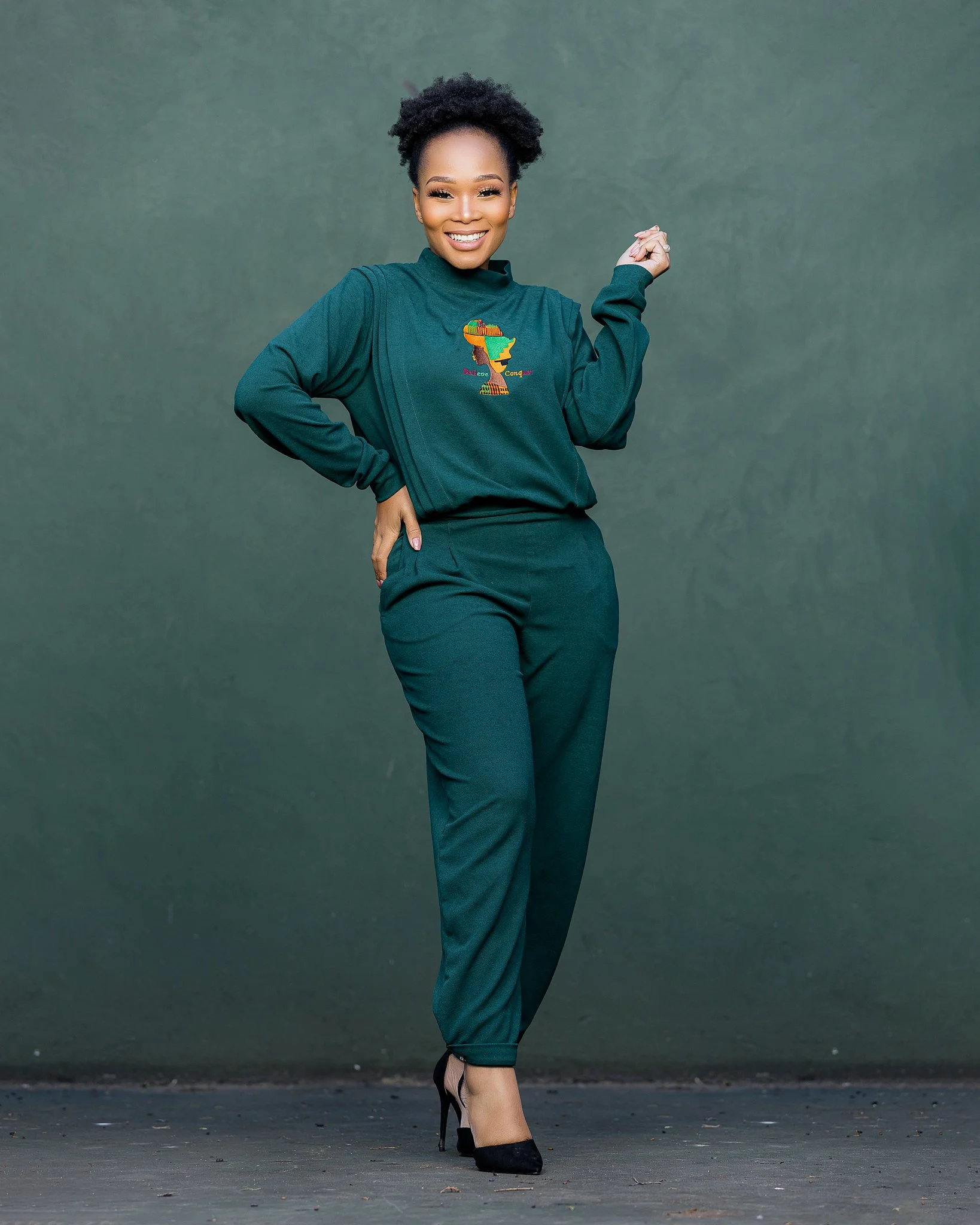 A woman in a green outfit standing and smiling against a green background.