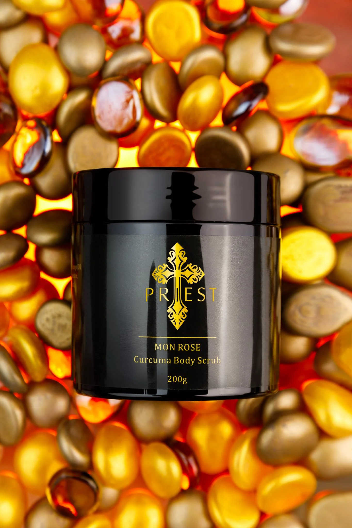 A black jar of Priest Mon Rose Curcuma Body Scrub placed on a colorful background of various stones.