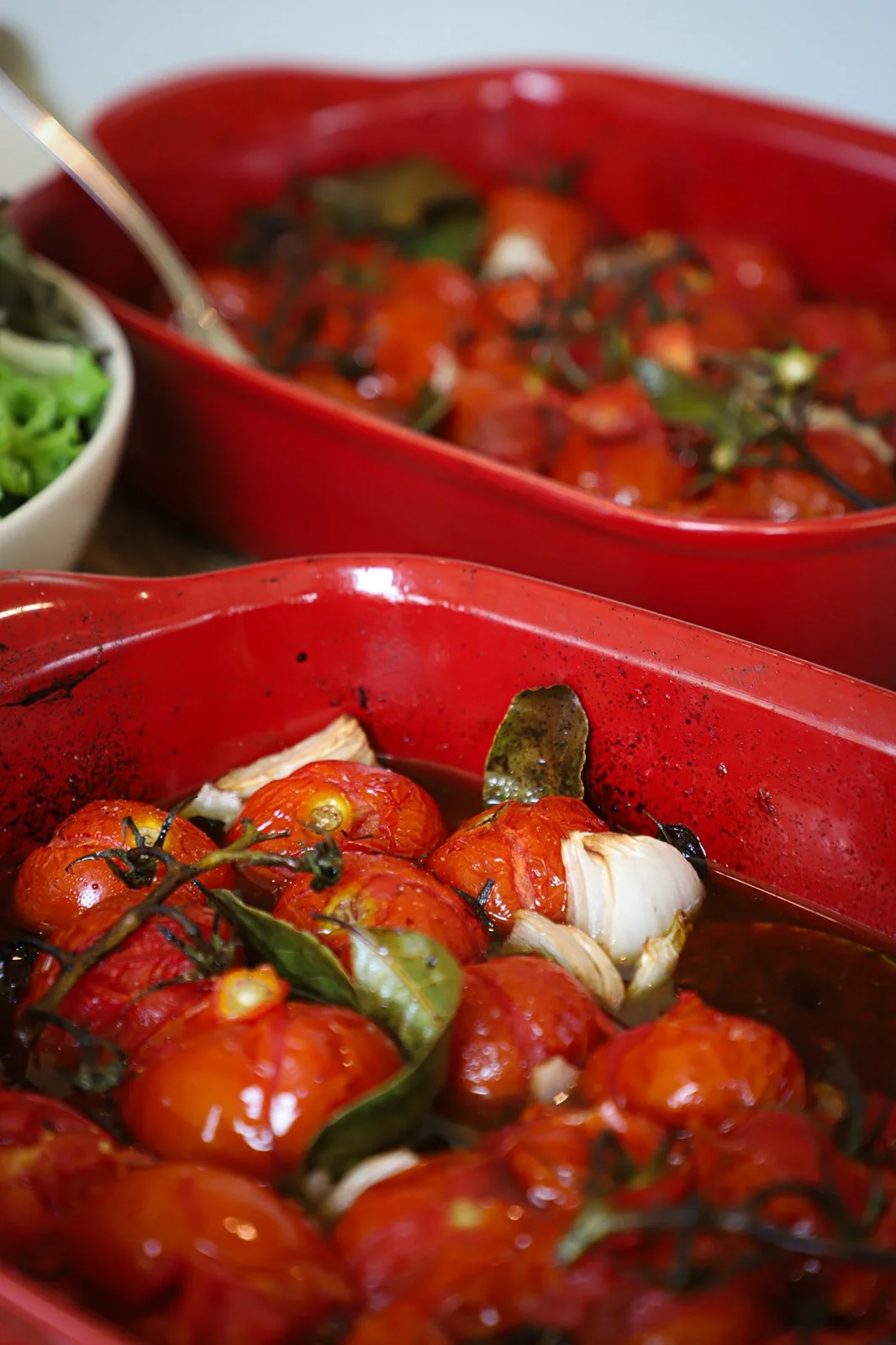 Roasted cherry tomatoes with garlic and herbs in a red baking dish.