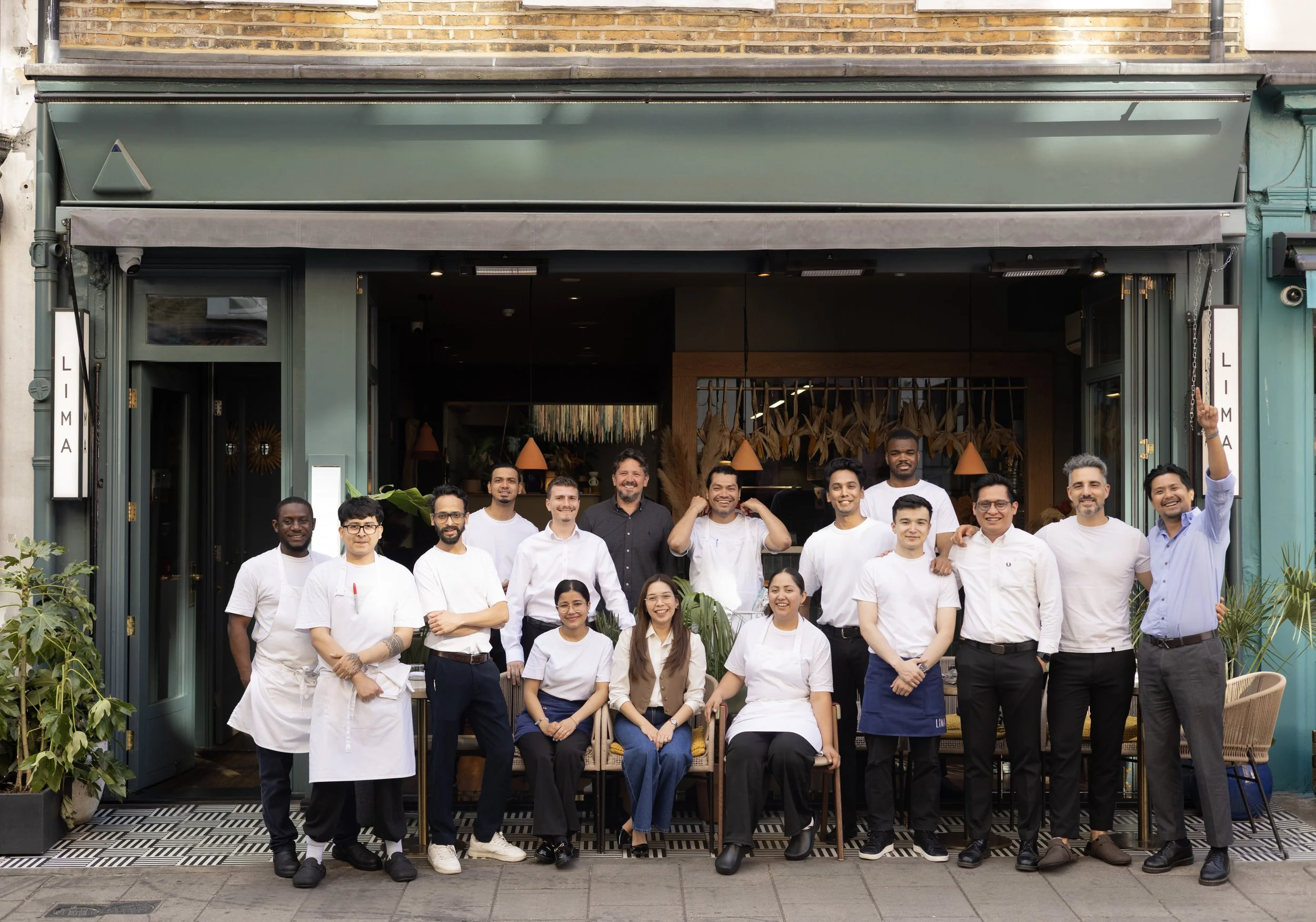 Lima team members, standing in front of a restaurant or cafe, smiling and posing for the photo. The building has a storefront with open doors and a sign on the side that reads 'LIMA'.