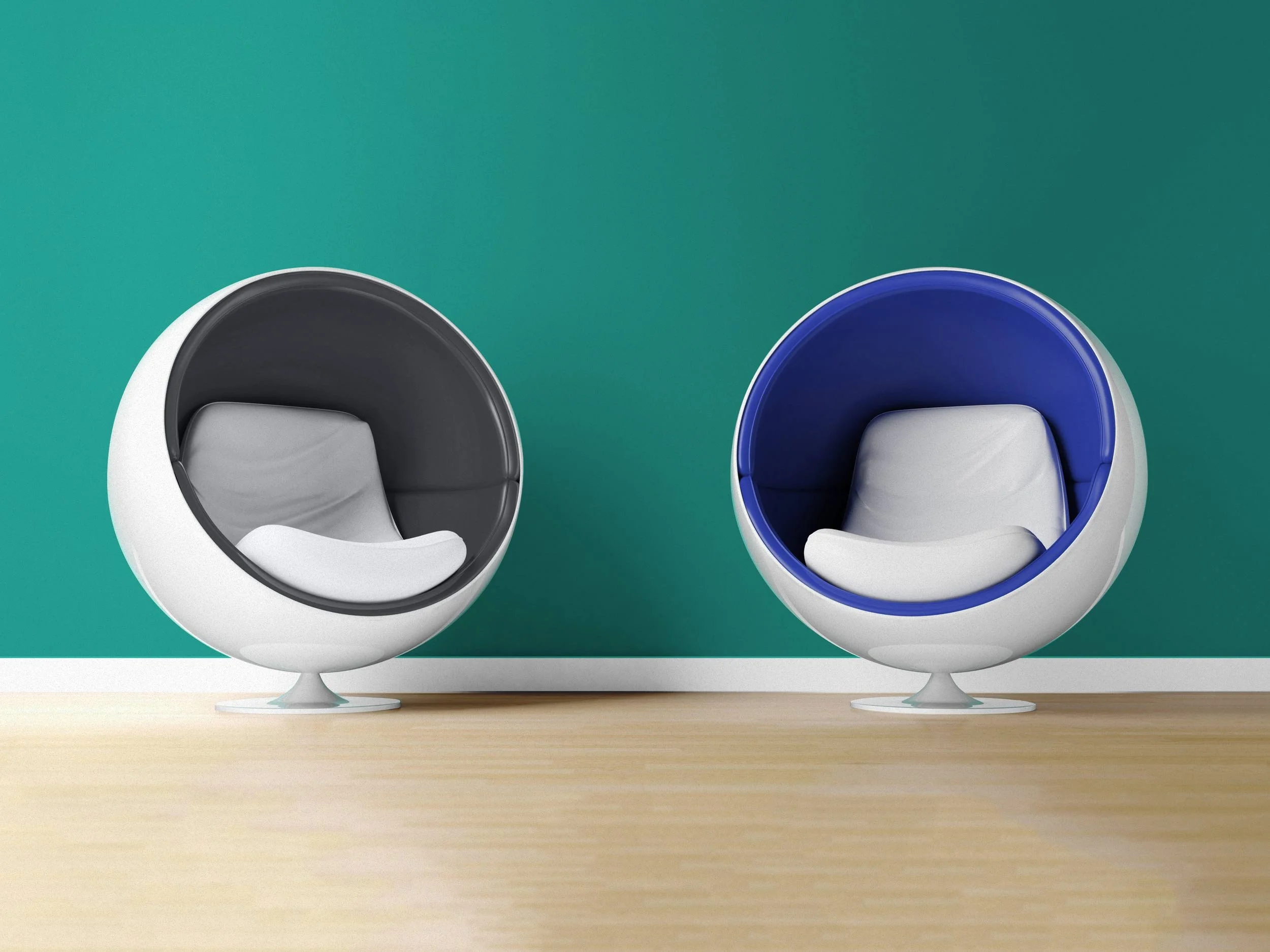 Two egg-shaped chairs with cushioned seats, one with a gray interior and the other with a blue interior, placed on a wooden floor against a teal wall.