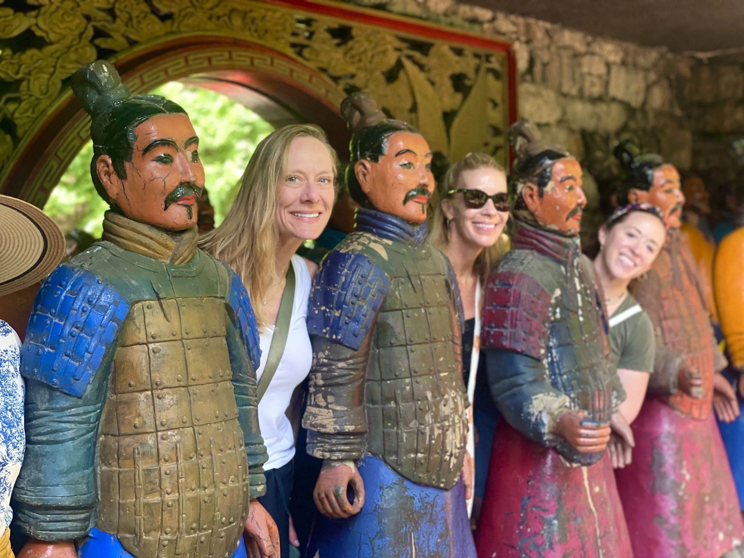 Tourists smiling and posing behind ancient Chinese Terracotta Warriors statues in a museum exhibit.