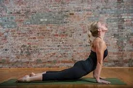 Woman practicing yoga in a cobra pose outdoors against a brick wall