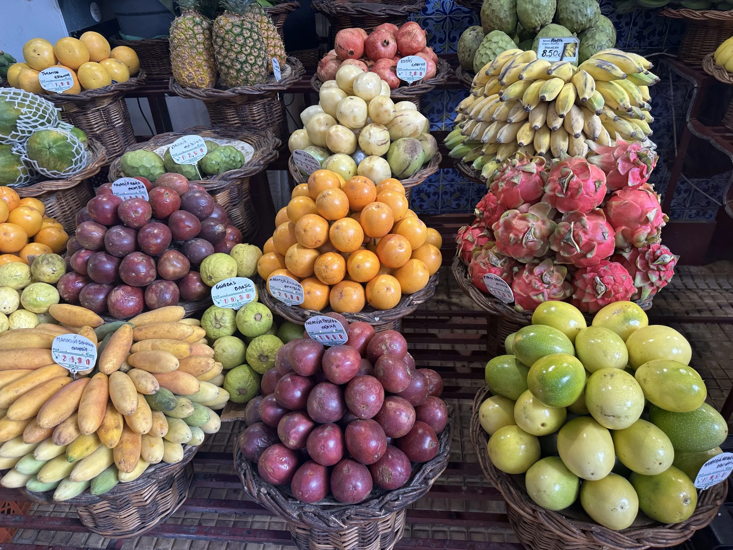 Assorted fruits in baskets at a market, including pineapples, pomegranates, bananas, dragon fruit, oranges, apples, lucuma, and other tropical fruits.