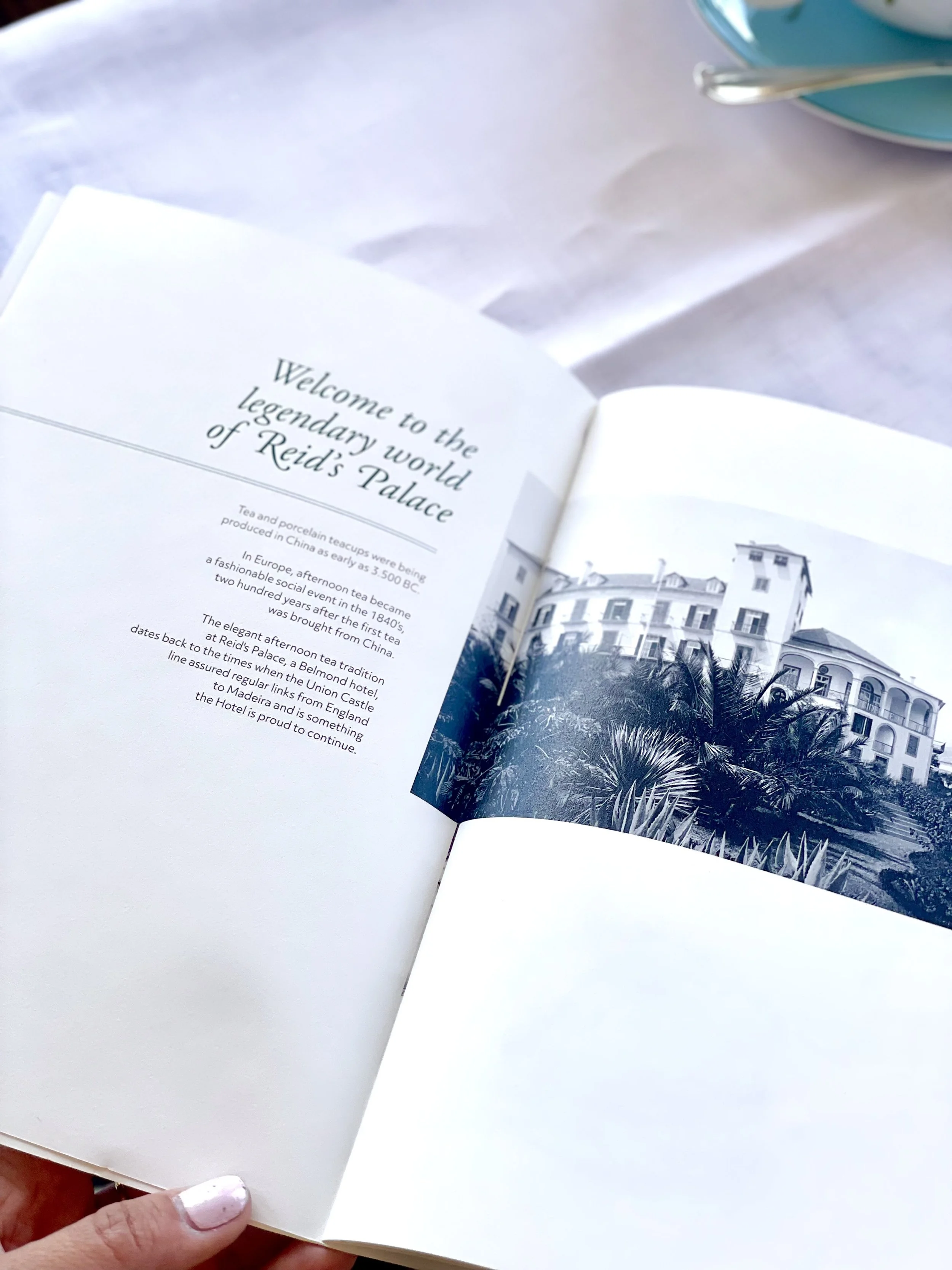 Open book with text and a black and white photo of a large ornate building surrounded by palm trees, placed on a light-colored table.