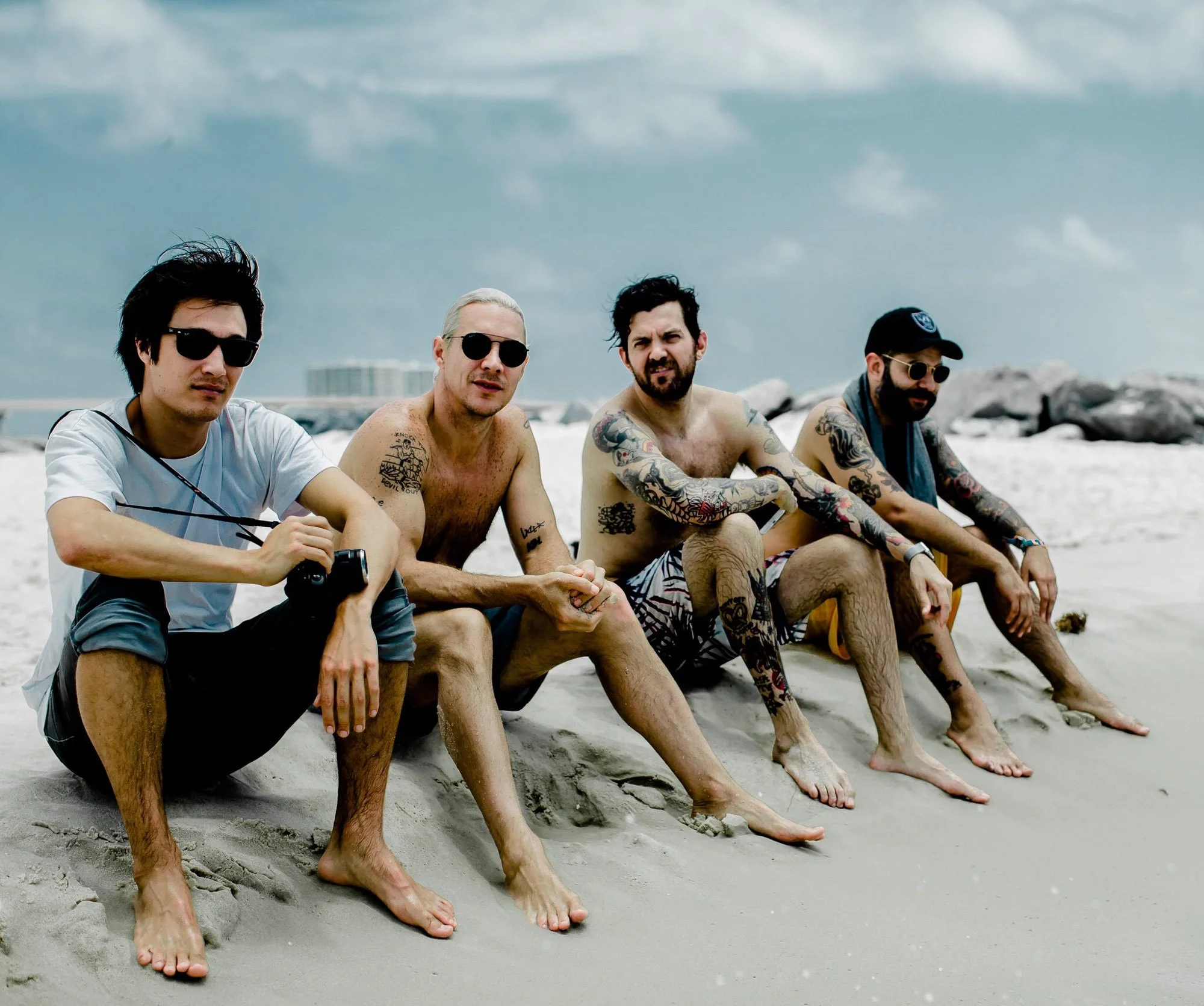  Group of four men sitting on a beach posing for the camera. 