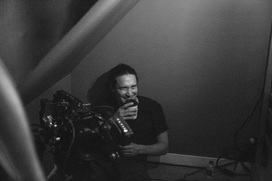  Cameraman smiling while operating a camera in a dimly lit room. 
