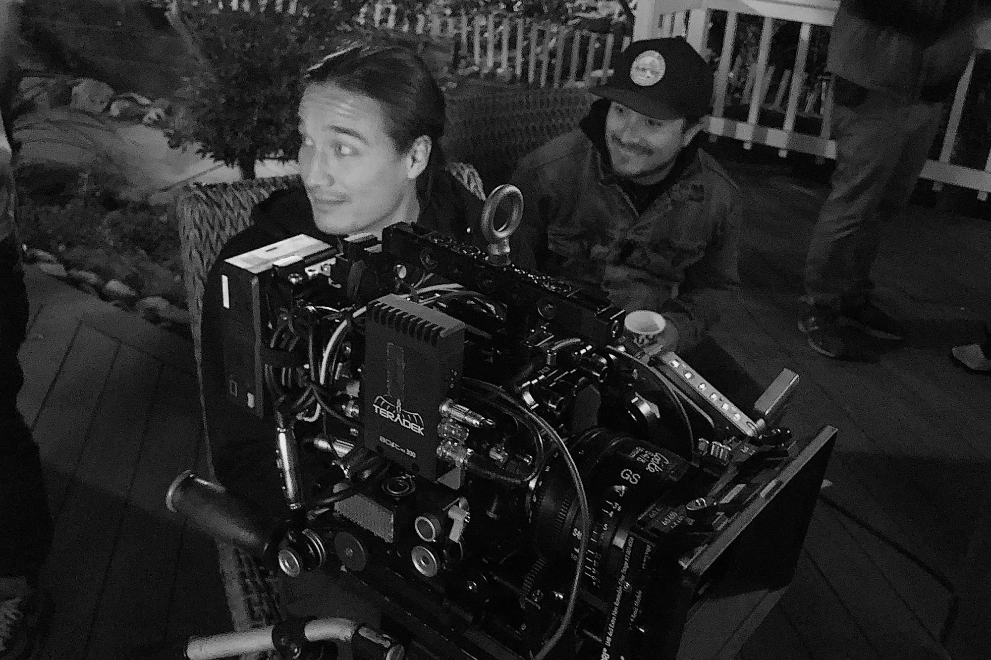  Two people smiling while sitting behind a camera setup during a nighttime shoot. 