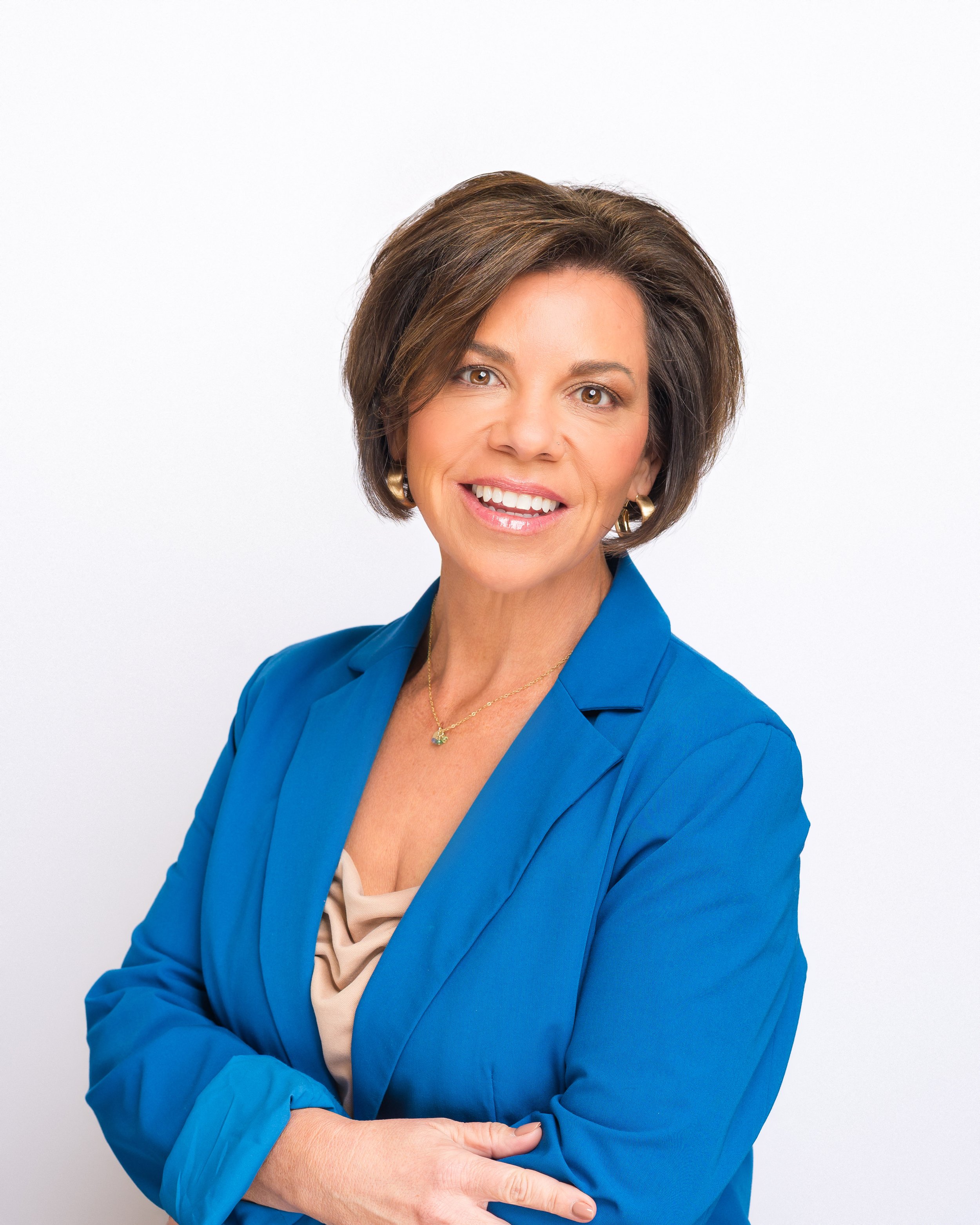 Professional woman with short brown hair wearing a blue blazer and a beige blouse, smiling at the camera.
