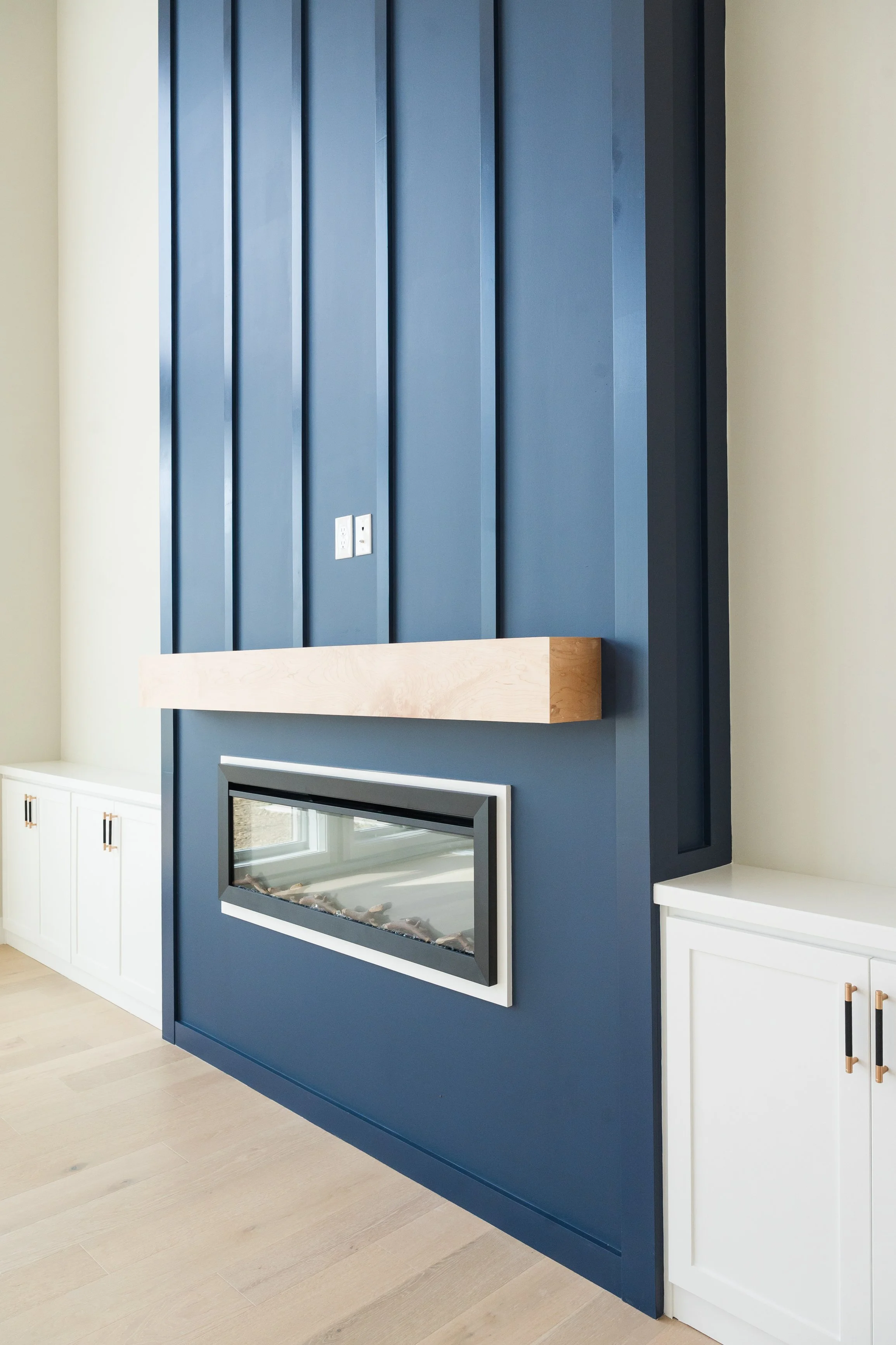 Modern living room with a blue accent wall, white cabinets, a wooden beam, a fireplace, and electrical outlets.