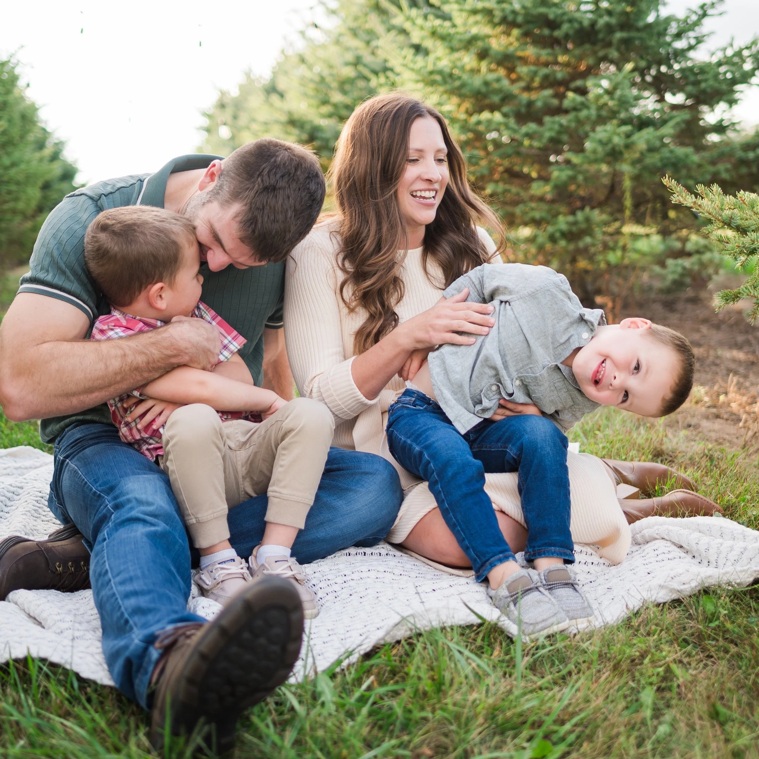 family of 4 sitting on ground amongst pine trees.