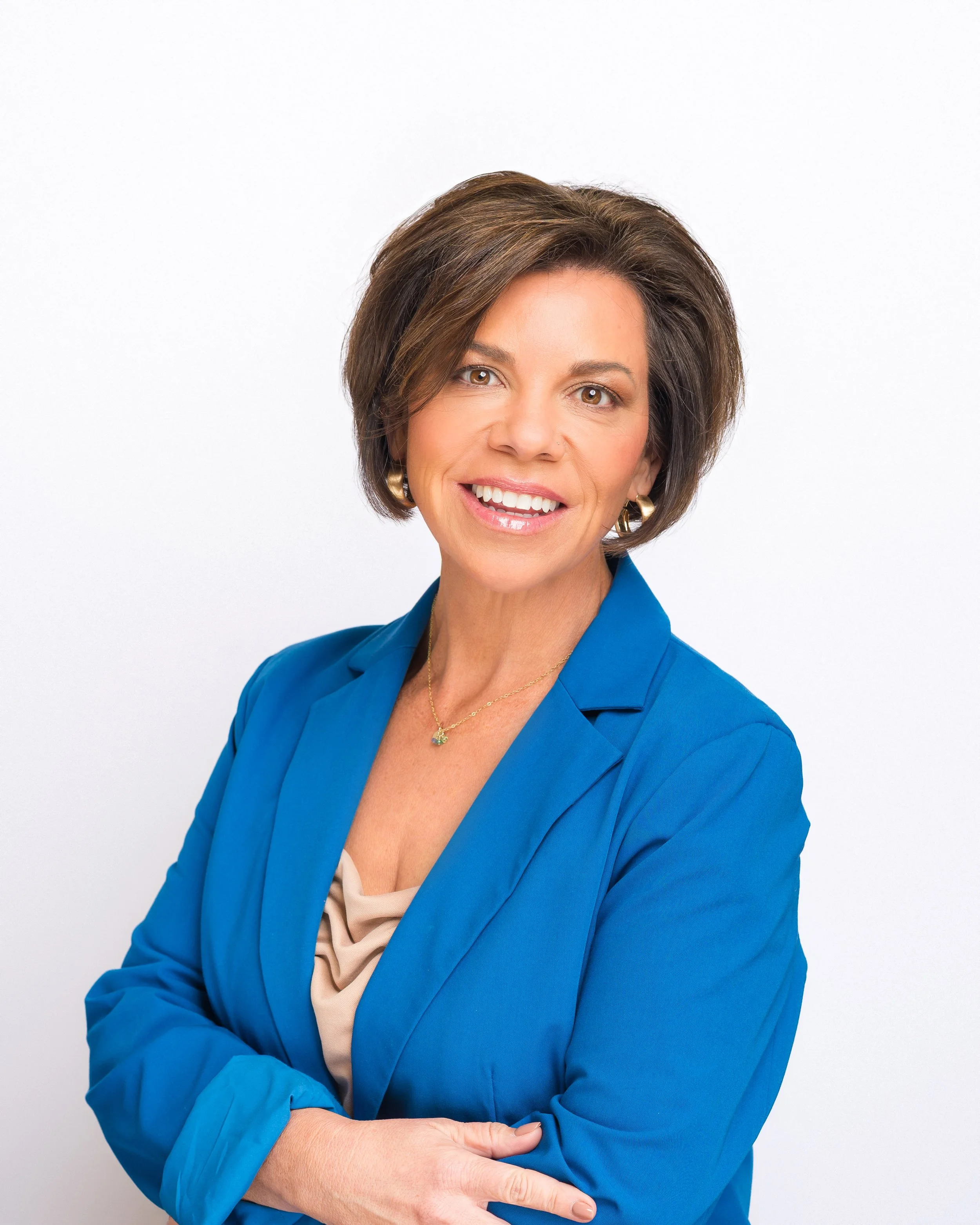 Professional woman in blue blazer smiling with arms crossed against a white background.