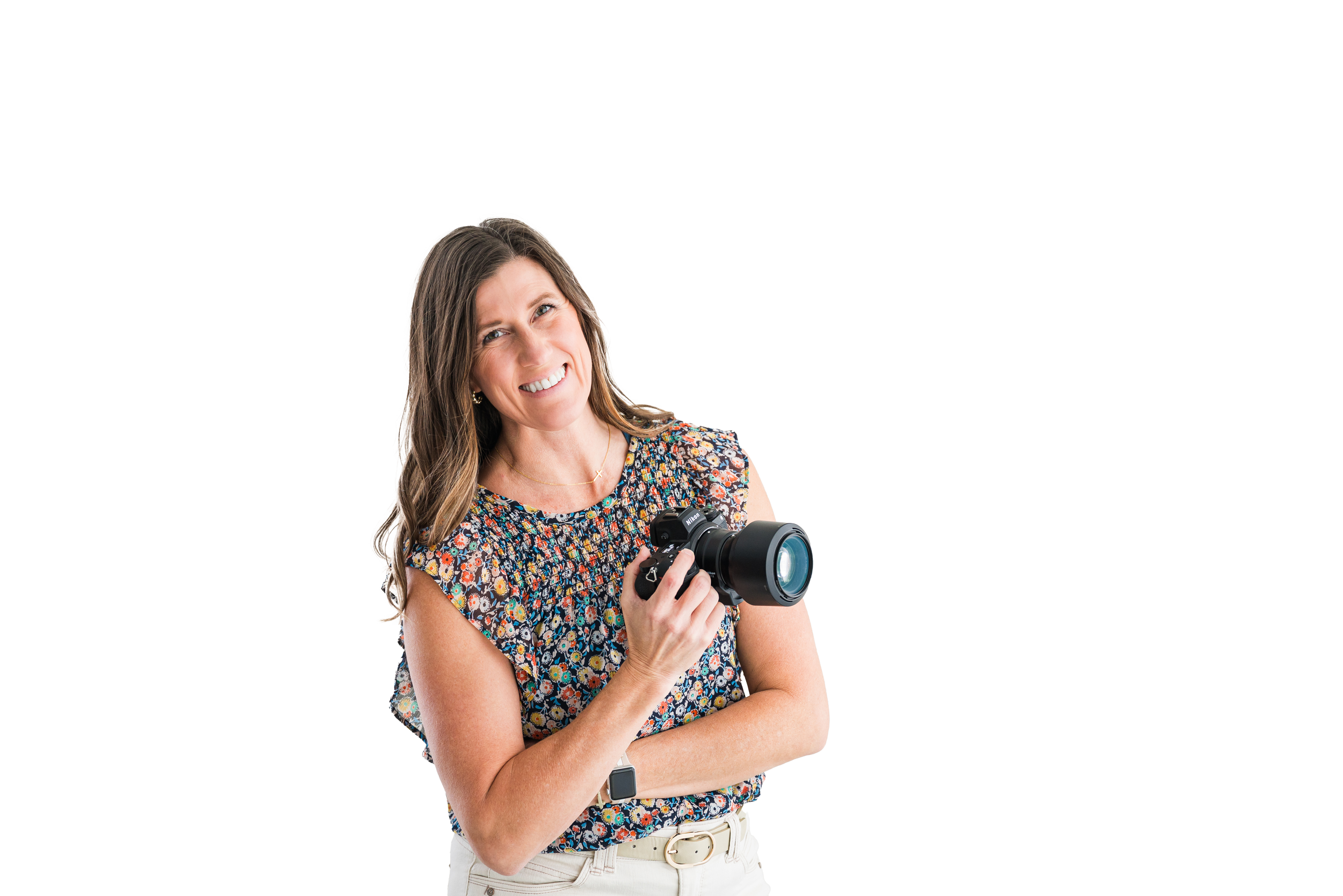 A woman with brown hair in a floral top holding a camera and smiling.