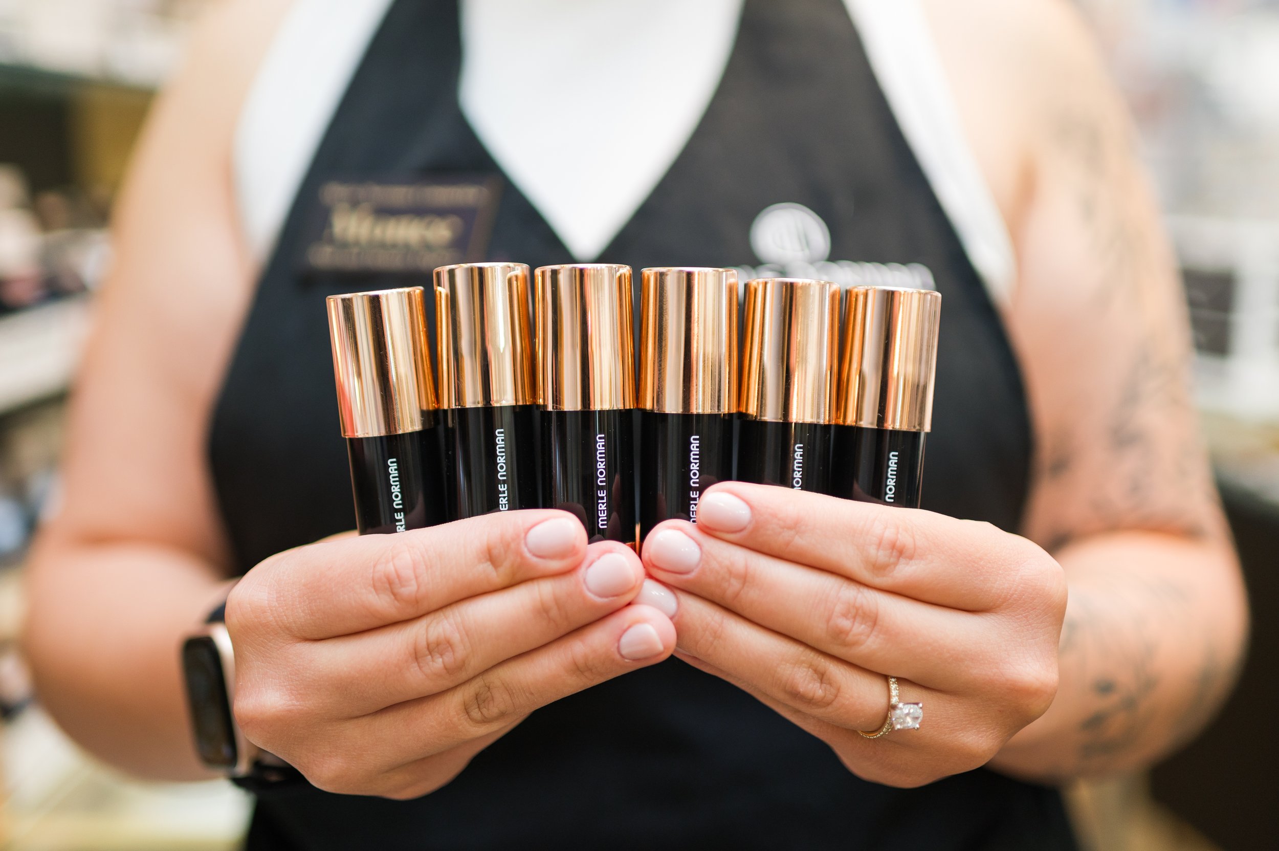 Person holding several black lipstick tubes with gold caps, wearing a black and white uniform, and a diamond ring on their finger.