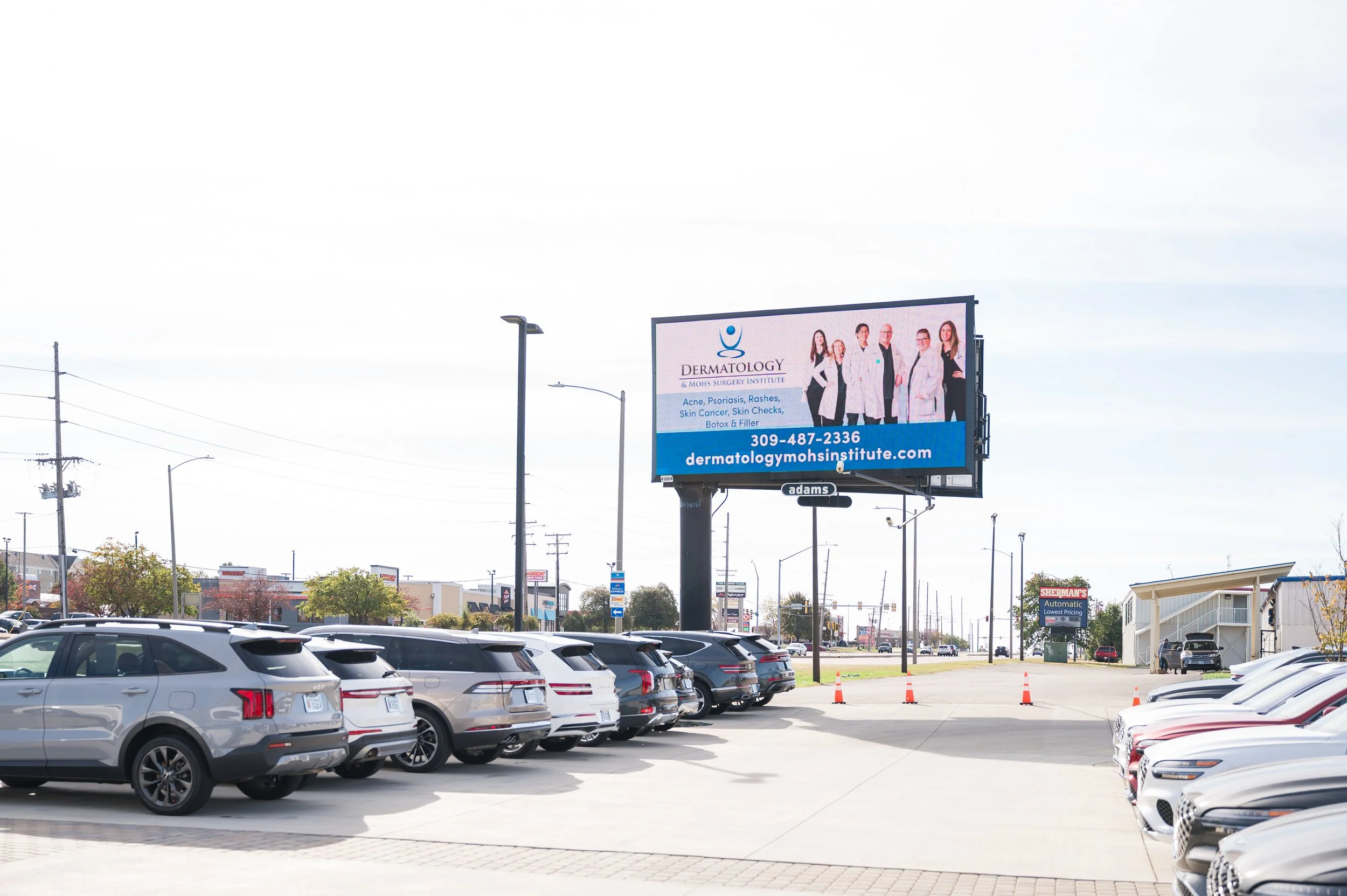 Parking lot with multiple parked cars, advertising billboard for a dermatology clinic, and a building in the background.
