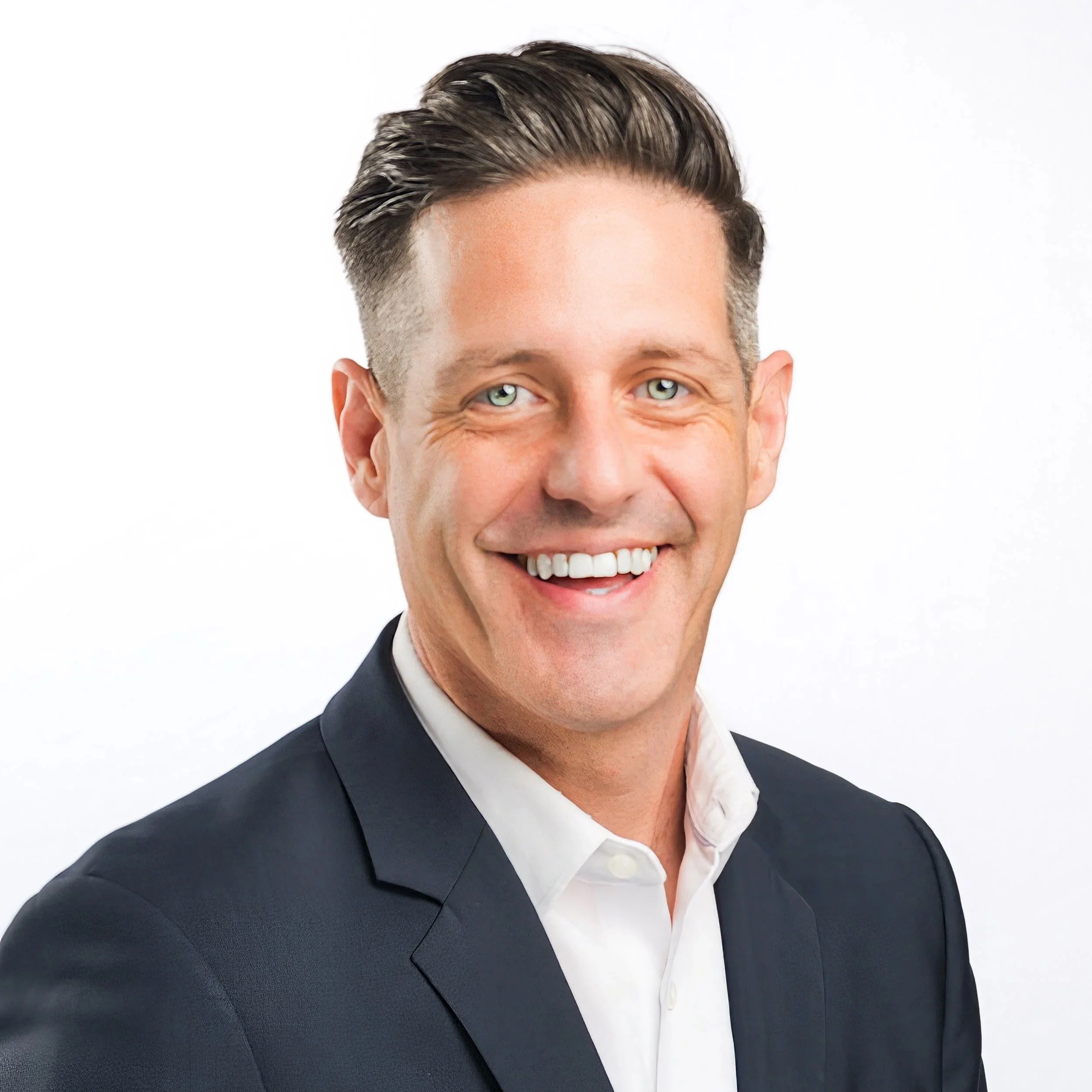 Headshot of a smiling man with short dark hair and blue eyes, wearing a dark suit and white shirt against a white background.