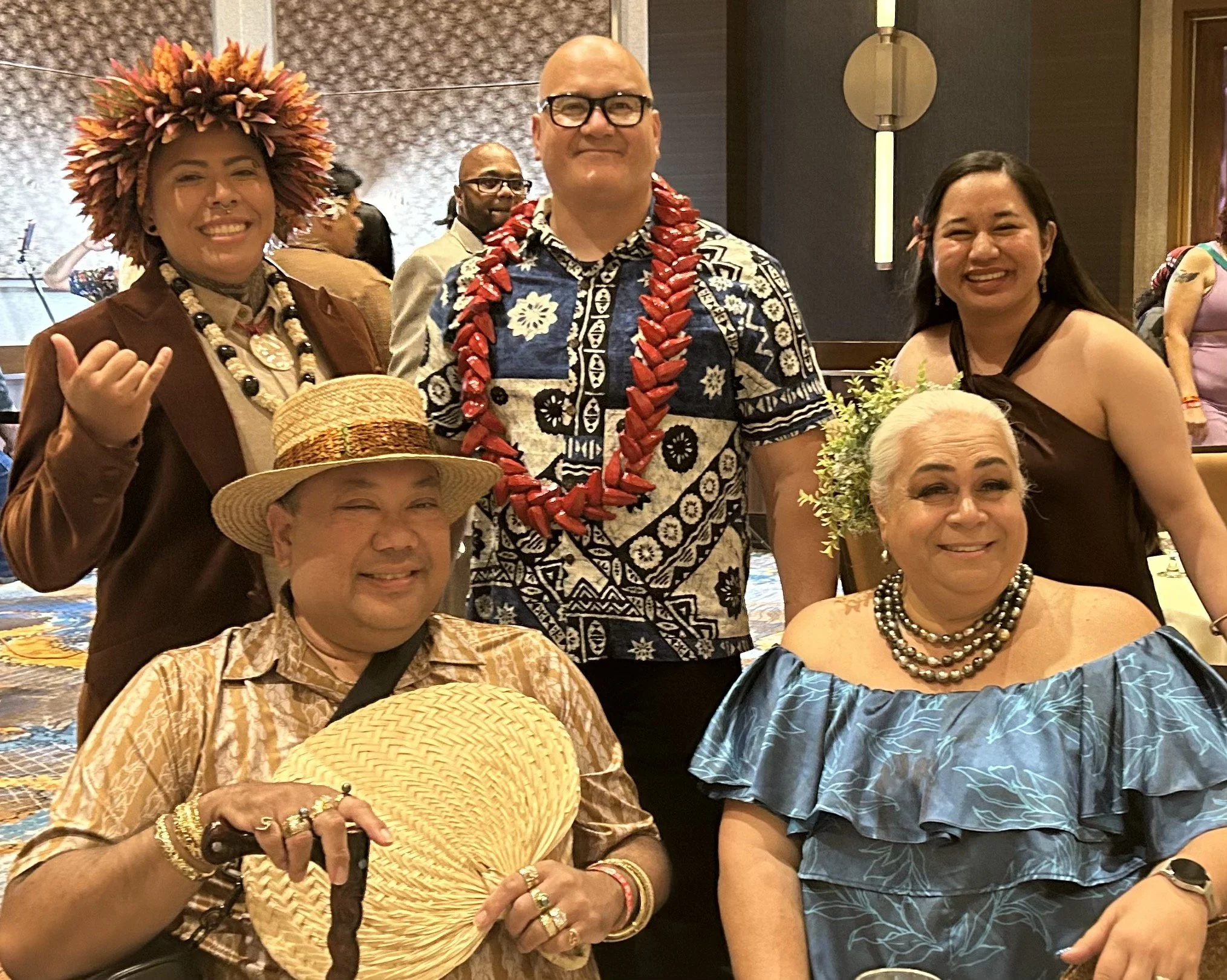 Five Pacific Islanders, three standing, two seated, pose together.