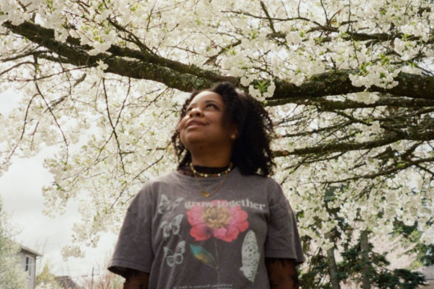 Tia Nettles stands beneath a cherry tree looking up at the white blossoms.