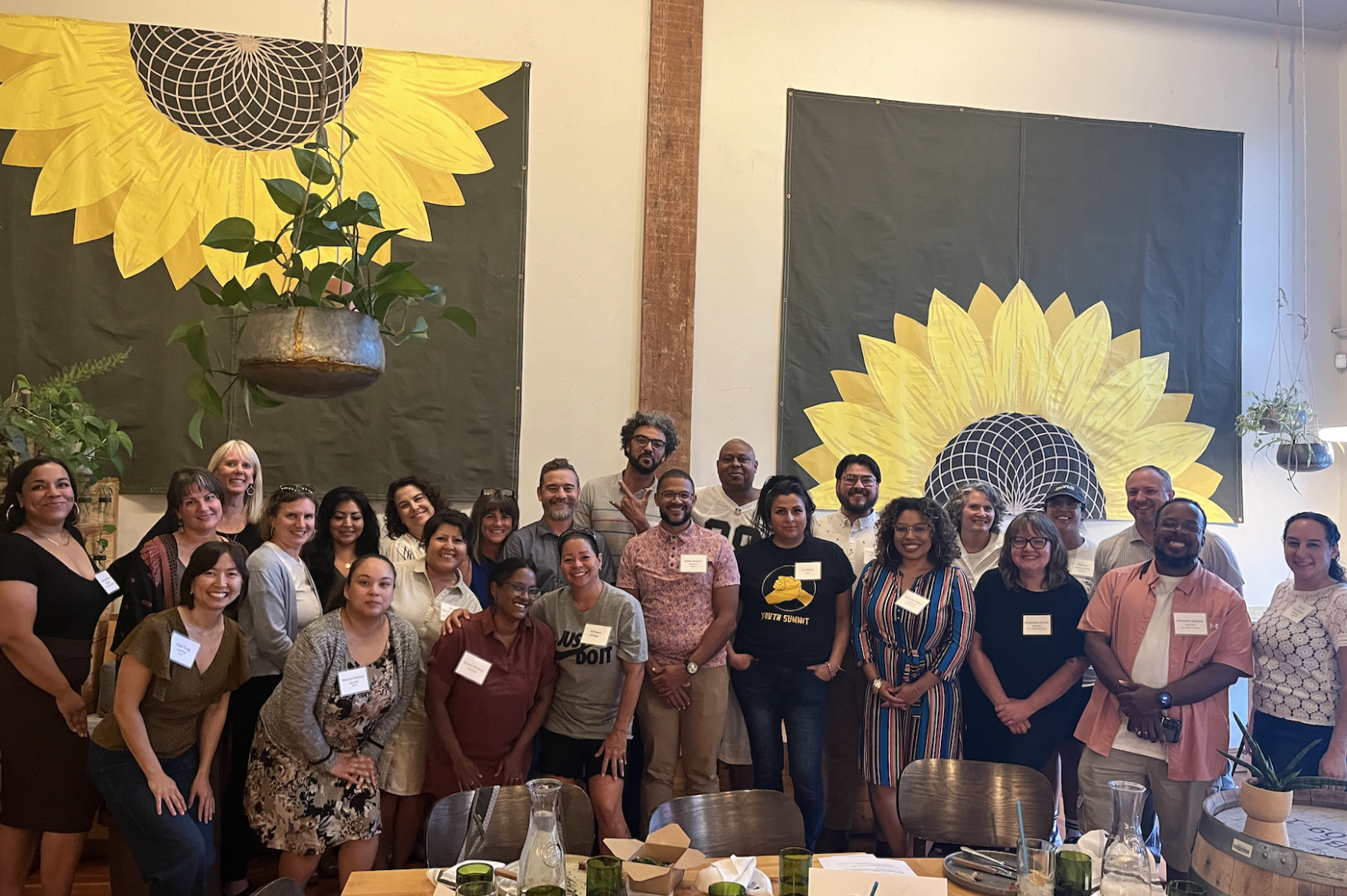 A couple dozen people wearing name tags pose in front of two large tapestries depicting sunflowers