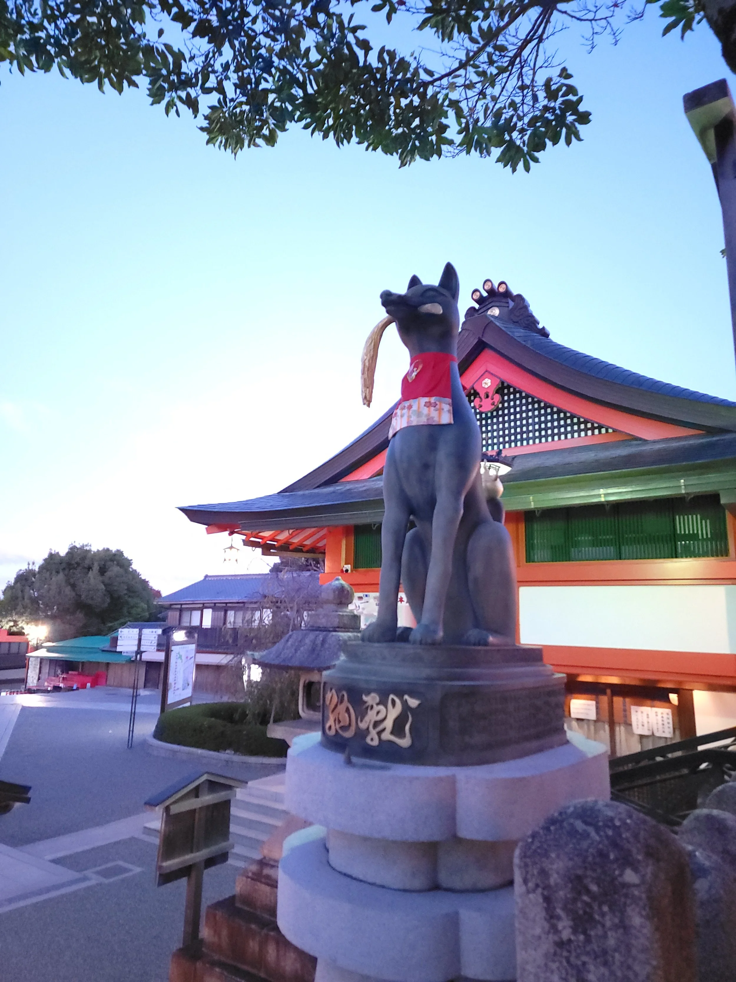 A well-maintained Inari statue with wheat in its mouth at the entrance to the main shrine.