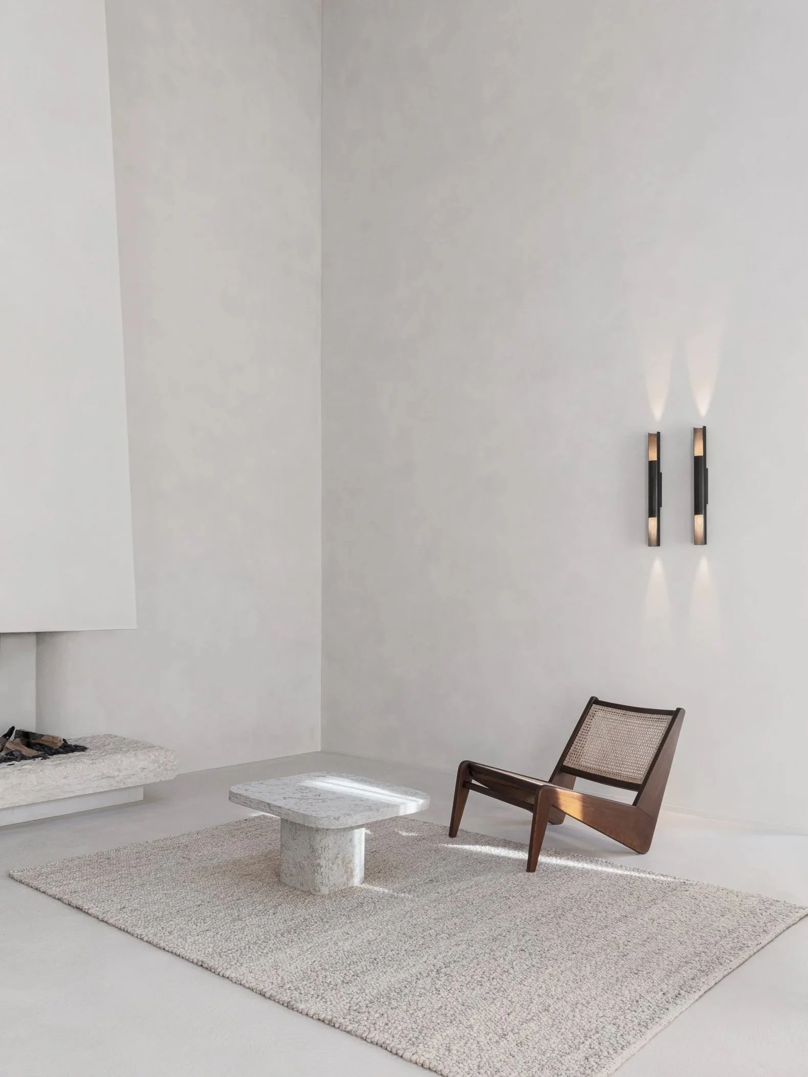 Minimalistic living room with a beige rug, a fondue table, a wooden chair, and wall-mounted lights.
