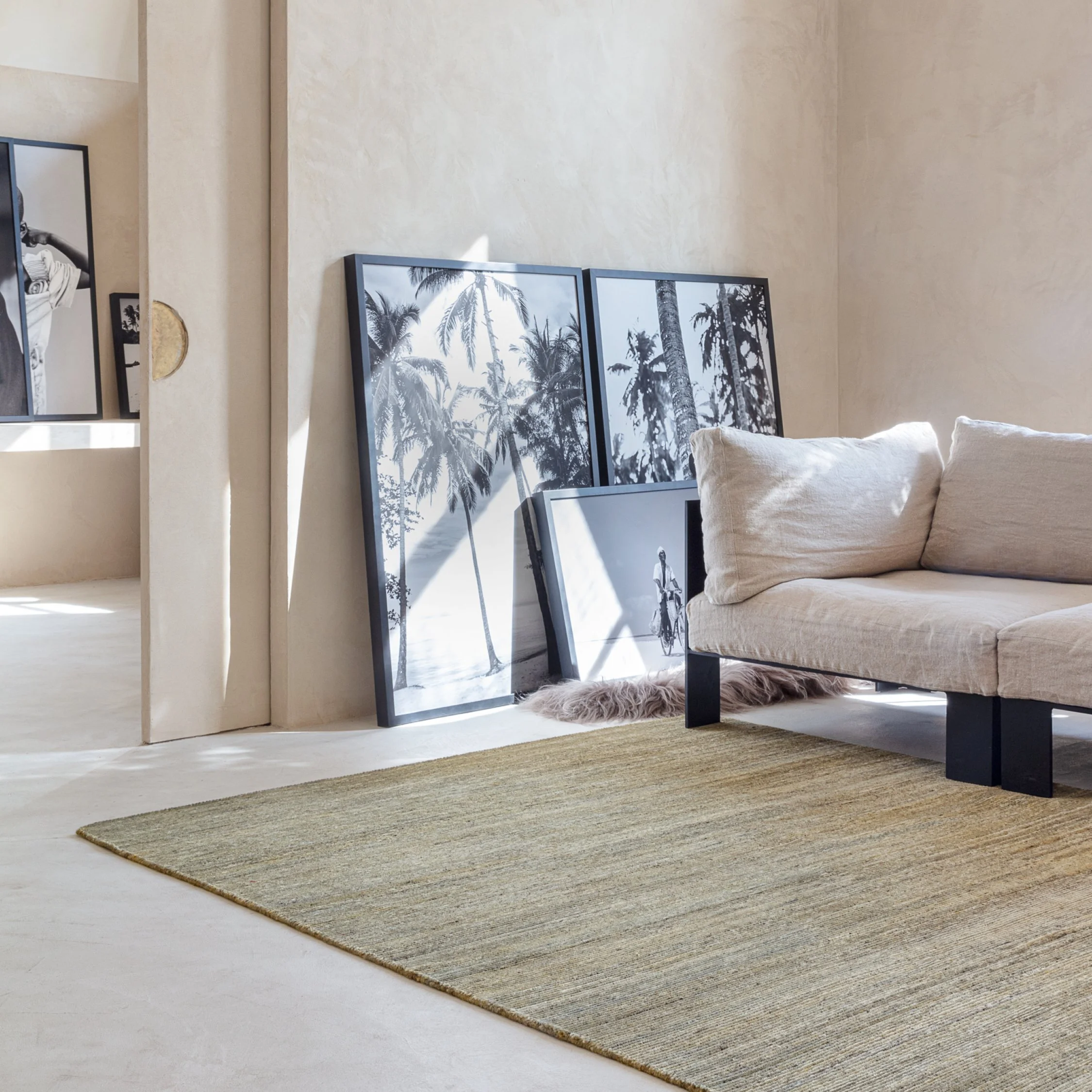 A beige living room with a beige sofa, a striped rug, and black and white tropical beach photos leaning against the wall.