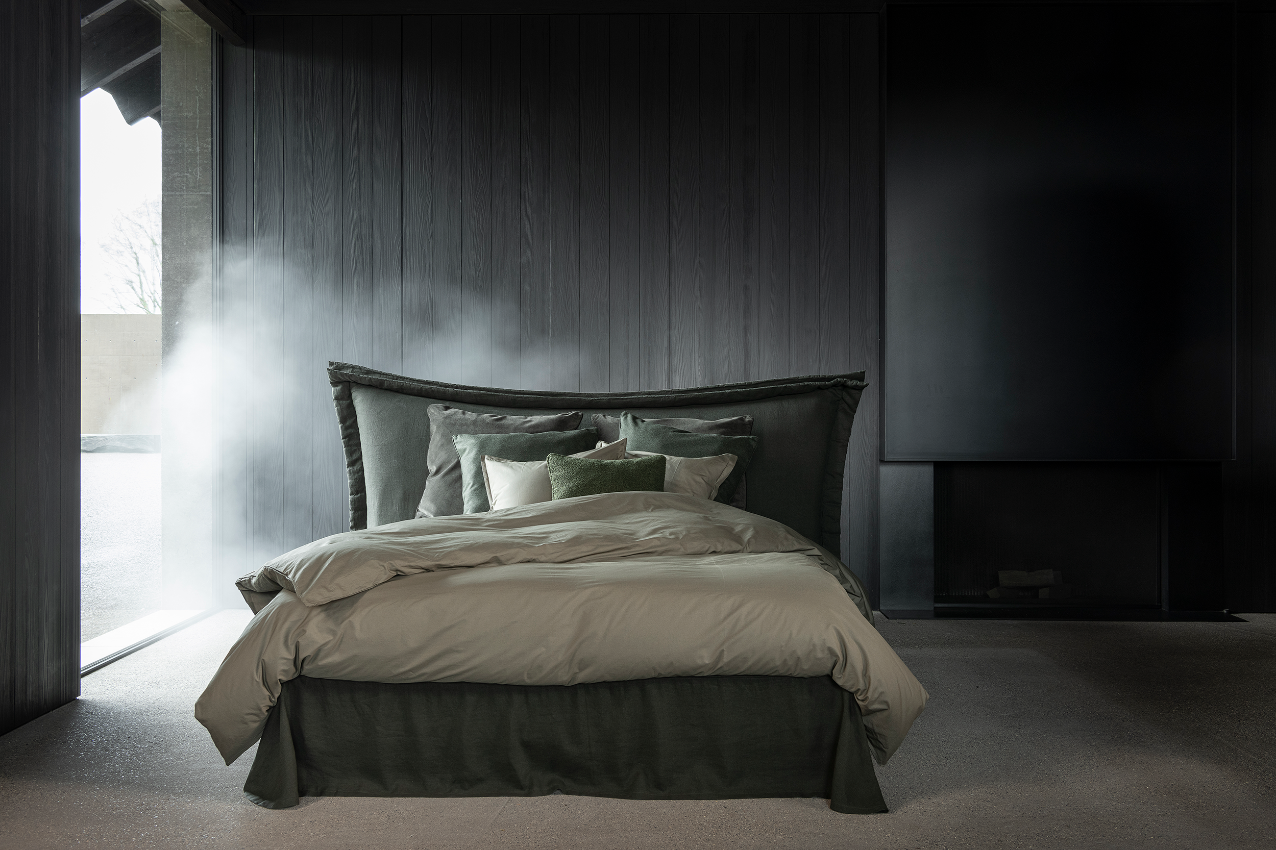 A modern bedroom with a dark wooden accent wall, a large bed with beige bedding, multiple pillows, and a built-in fireplace.