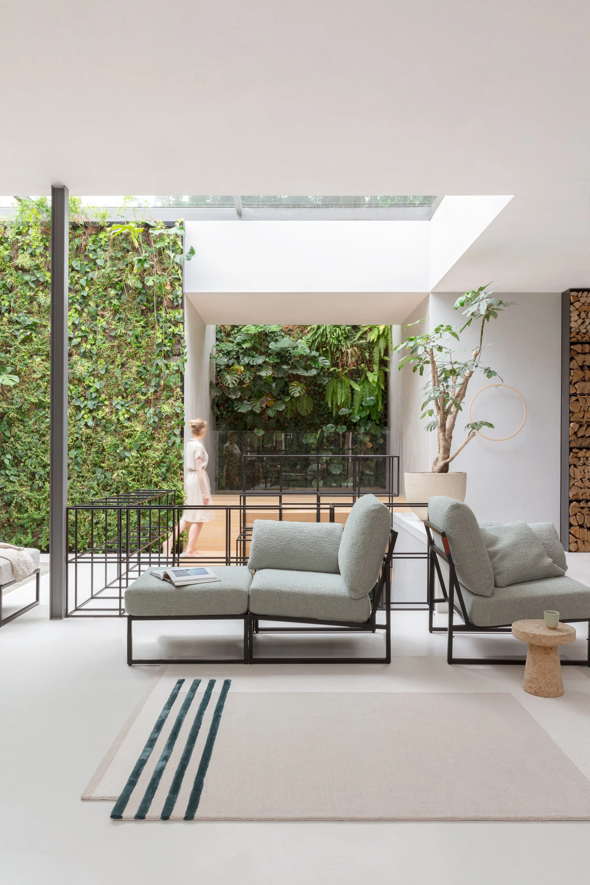 Modern living room with white walls, gray sectional sofa, potted plant, and view of a green wall through an opening.