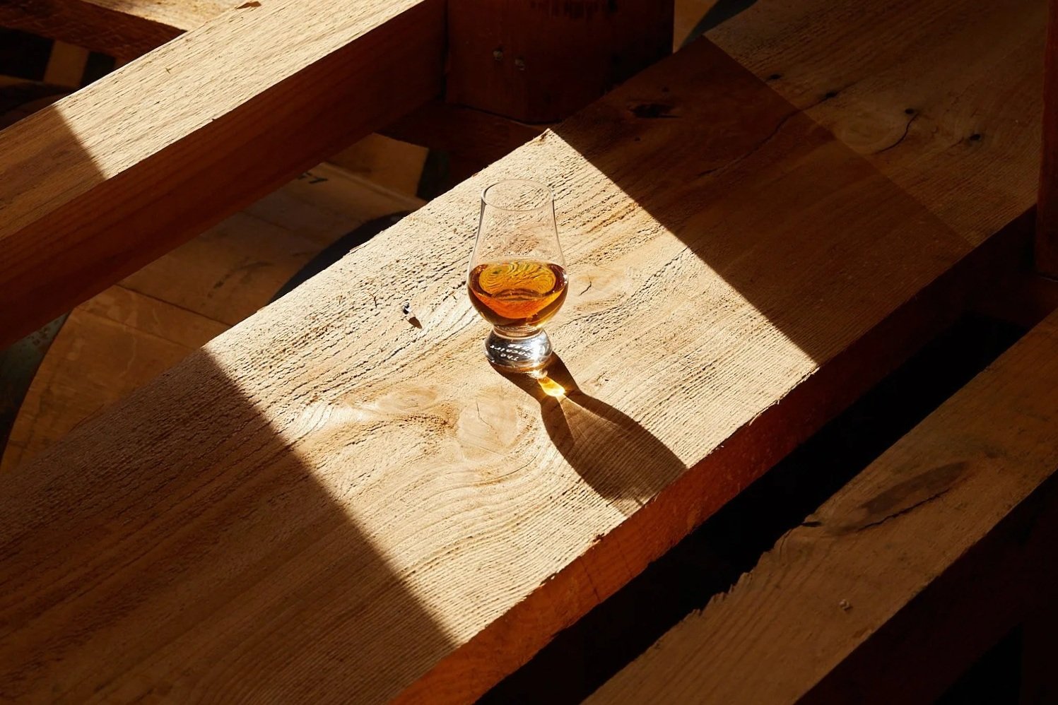 Glass of bourbon resting on wooden distillery beams in warm natural light, photographed on location in Kentucky.