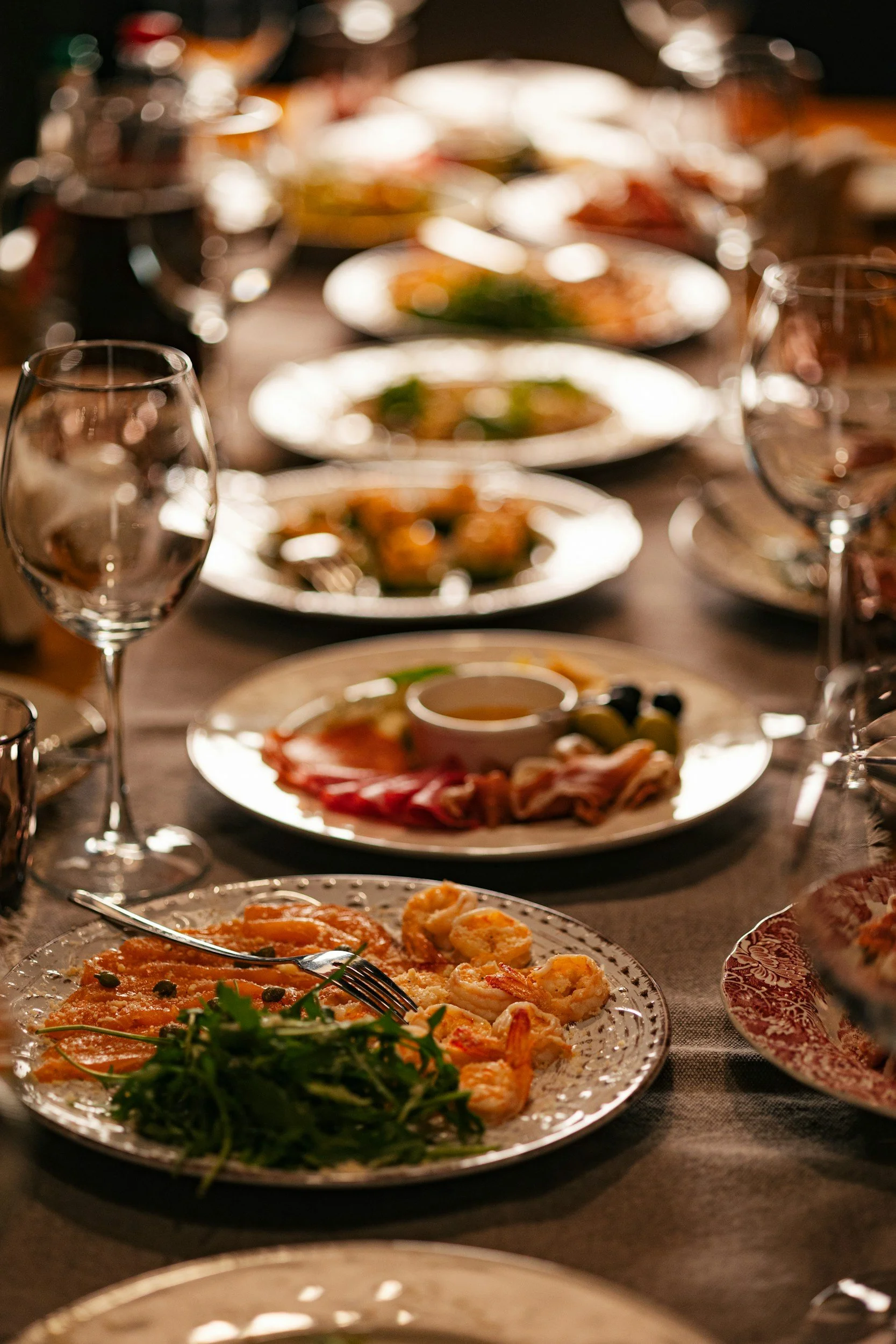 A group dining table set for a meal with various dishes and multiple wine glasses.