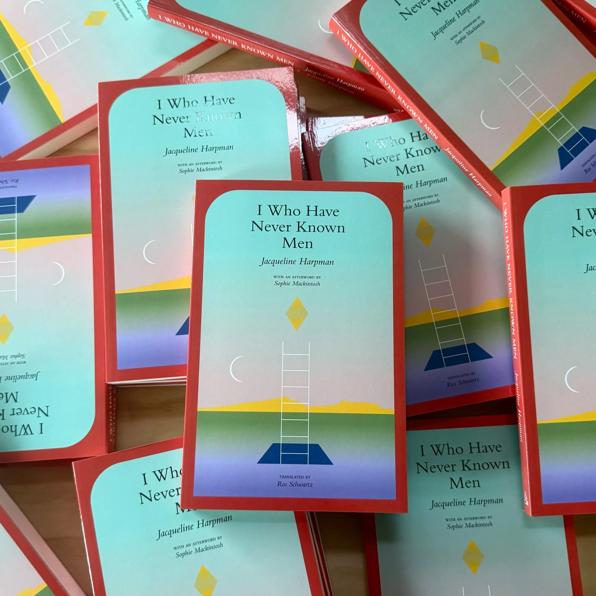 Pile of books on table for I Who Have Never Known Men. The book cover is an abstract graphic of a ladder rising from a void-like hole in the ground