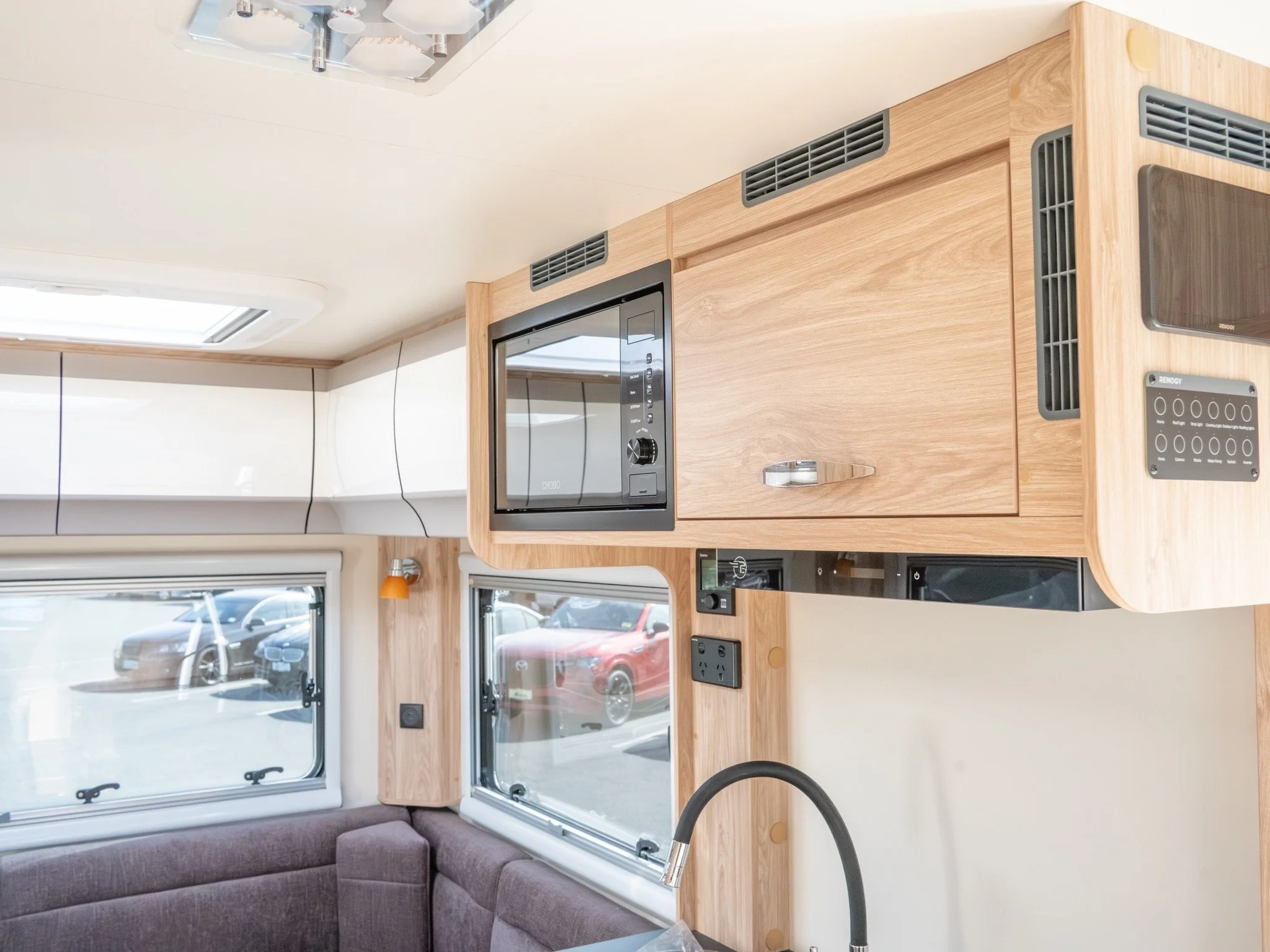 Interior of a tiny home or camper with wooden cabinetry, a microwave, a window, and a dark gray sofa.