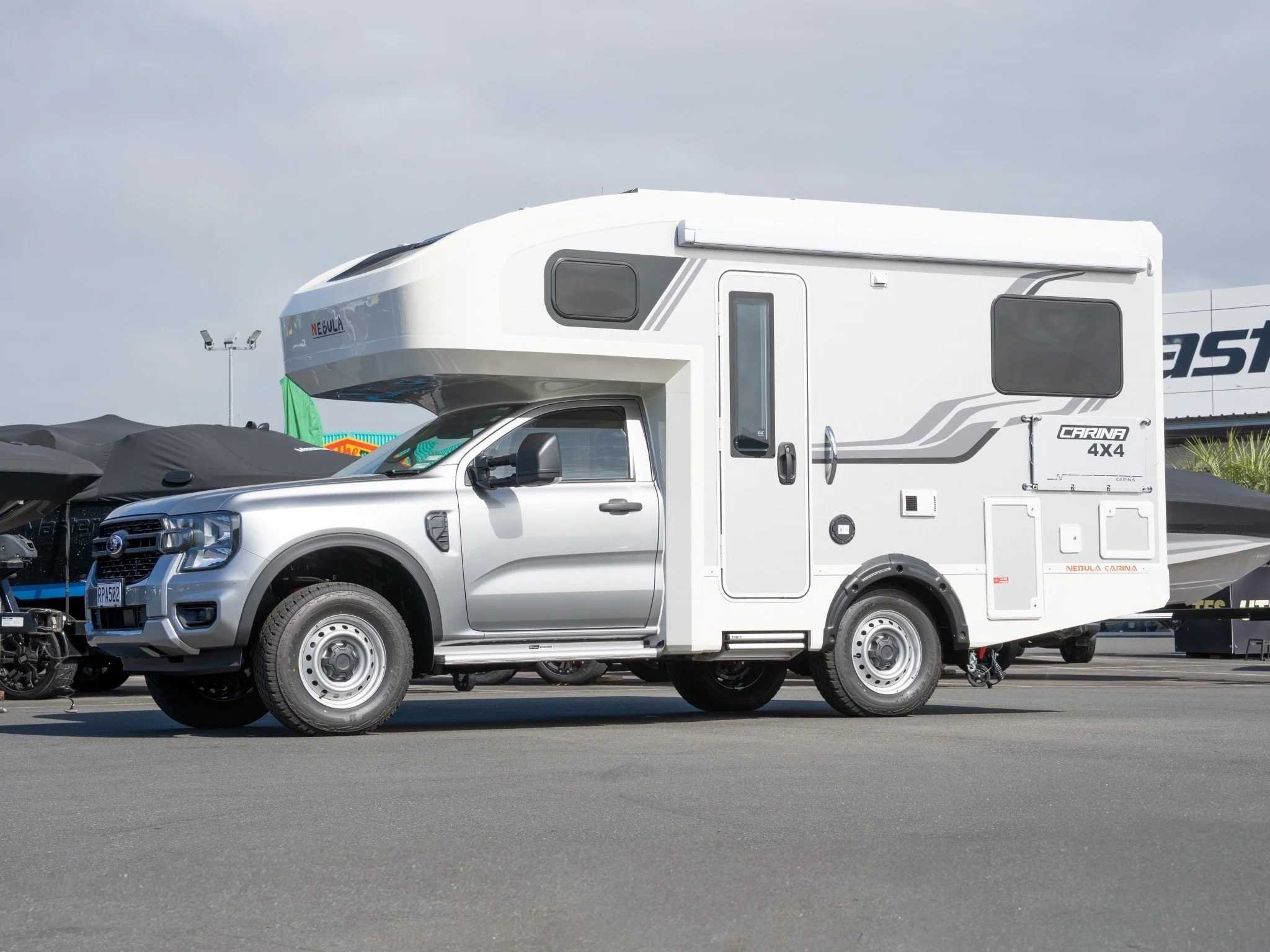 Silver Ford pickup truck towing a white caravan RV with gray and black accents parked in an outdoor lot on a cloudy day.