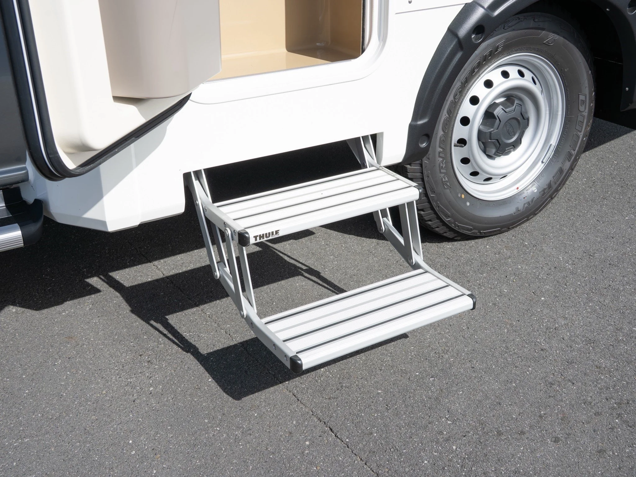 Close-up of a large tire and a vehicle step with a foldable metal ladder positioned outside a white truck with an open door.