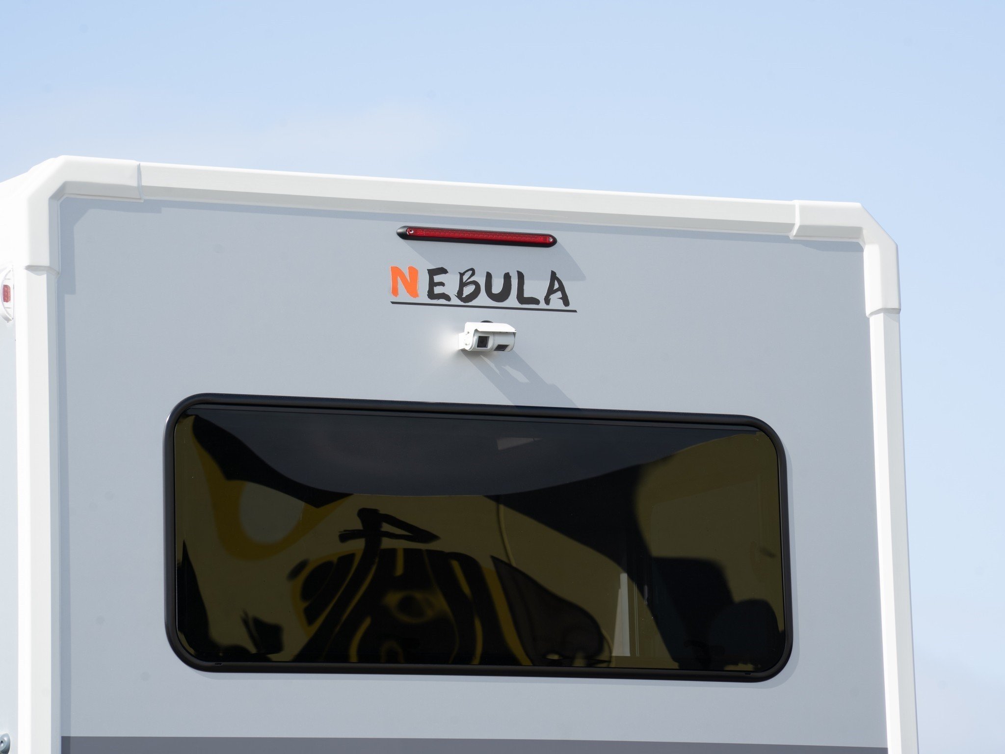 Close-up of the rear of a white vehicle with a sign that says "Nebula" and a graphic of a yellow nebula inside a black screen, set against a clear blue sky.