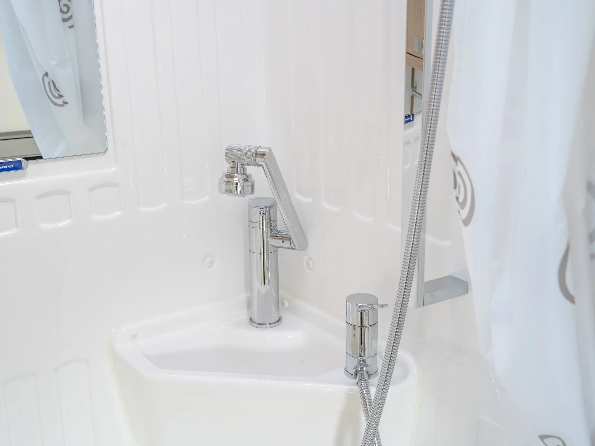 Close-up of a chrome faucet with a matching soap dispenser and a flexible shower hose in a white bathroom sink area.