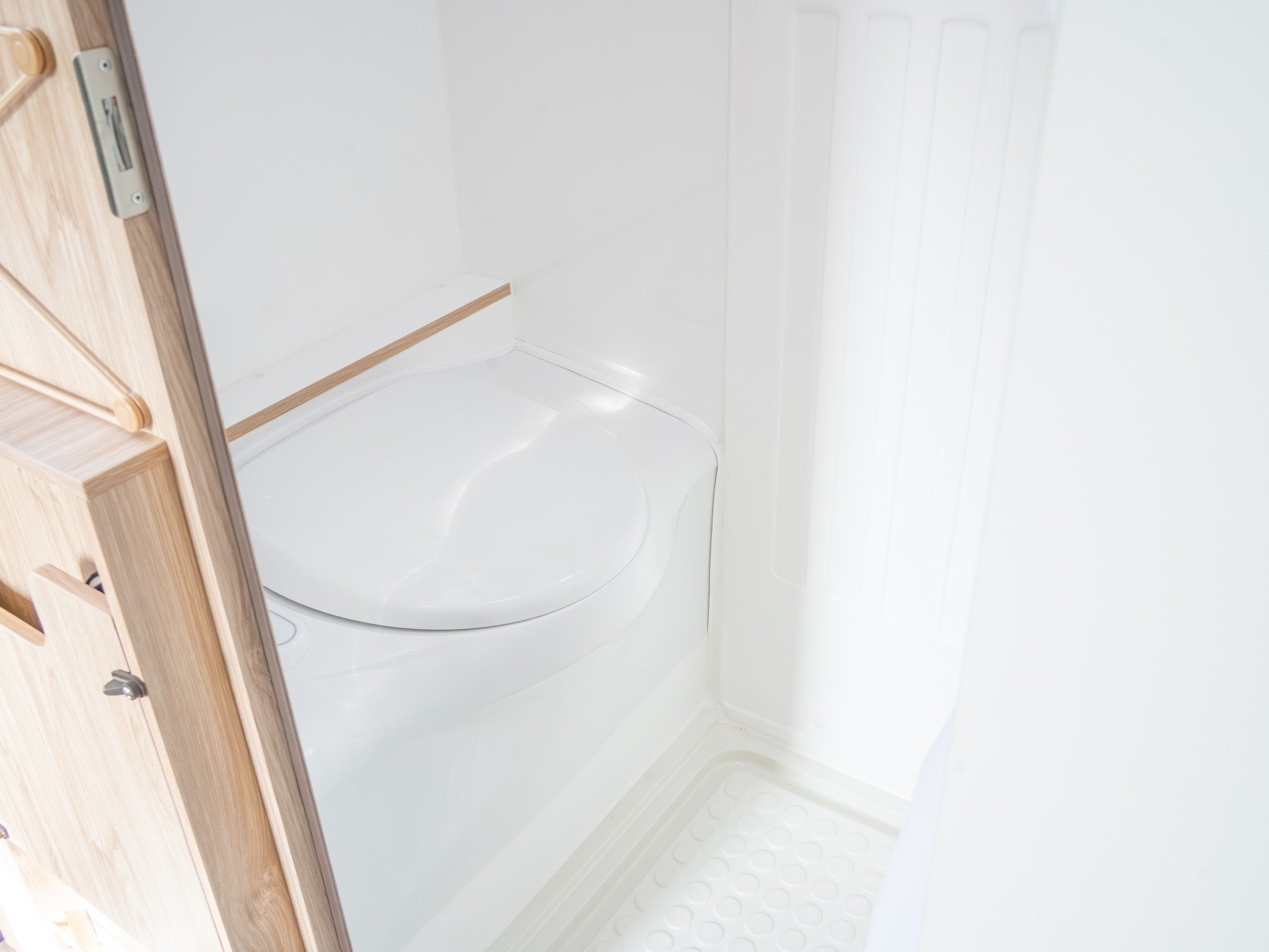 Interior view of a small shower stall with white walls, a textured white shower base, and a wooden door frame.