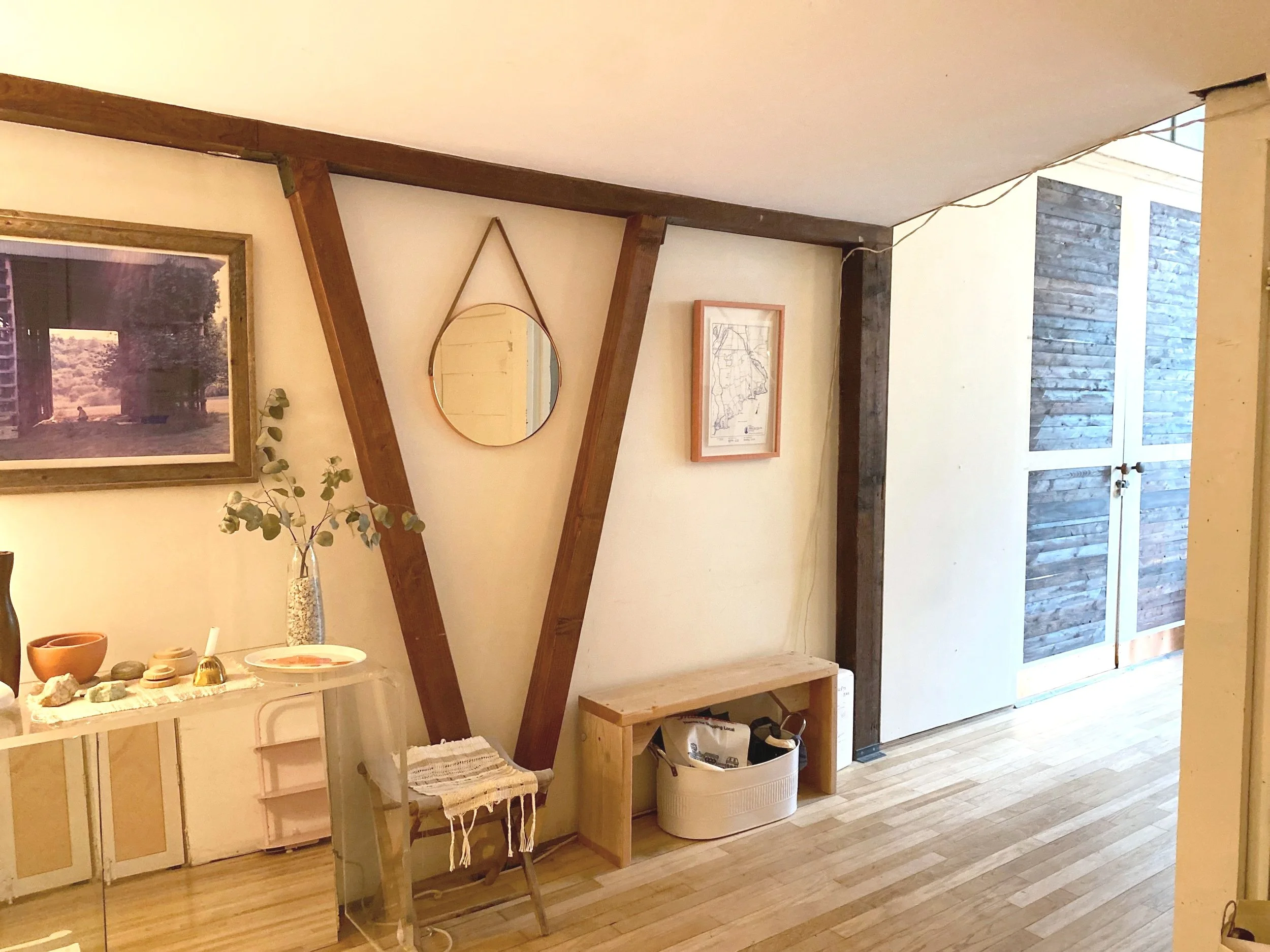 Interior of a cozy room with wooden accents, framed pictures, a shelf with decorative items, and a small bench.