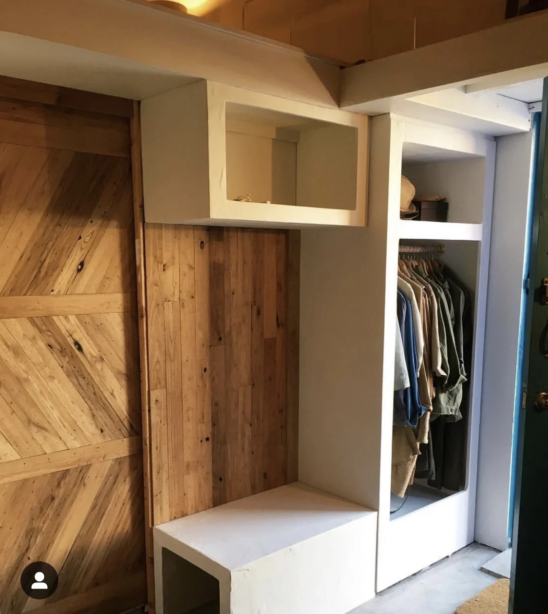 Built-in white closet with hanging clothes and open shelving, adjacent to a wooden door with diagonal planks.