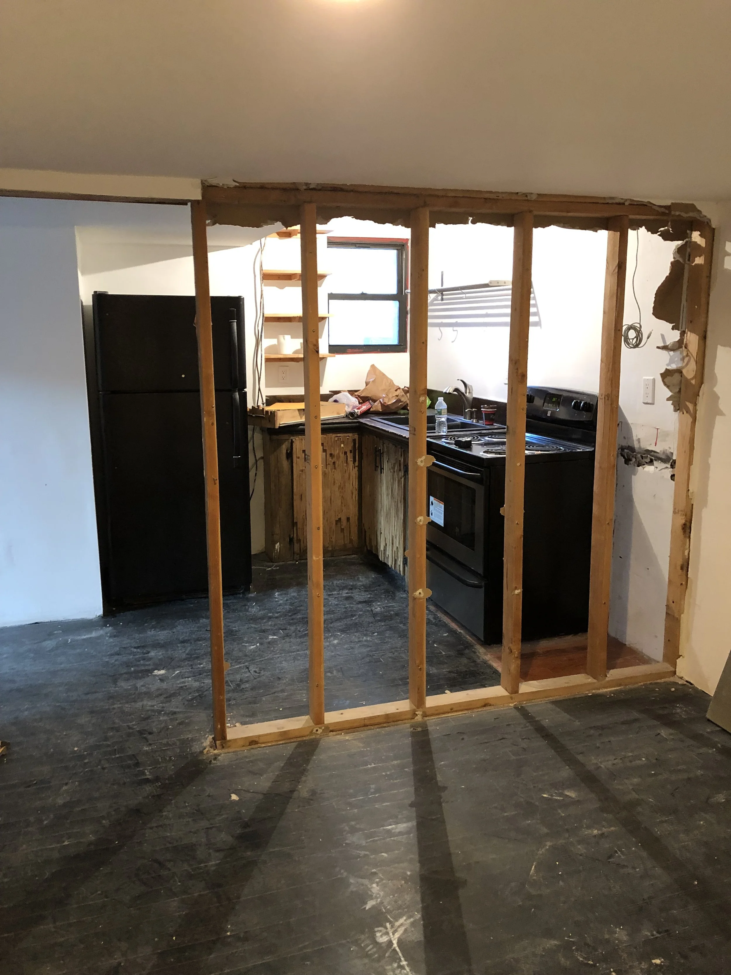 Partial wall removal in a kitchen, exposing wooden studs and framing.