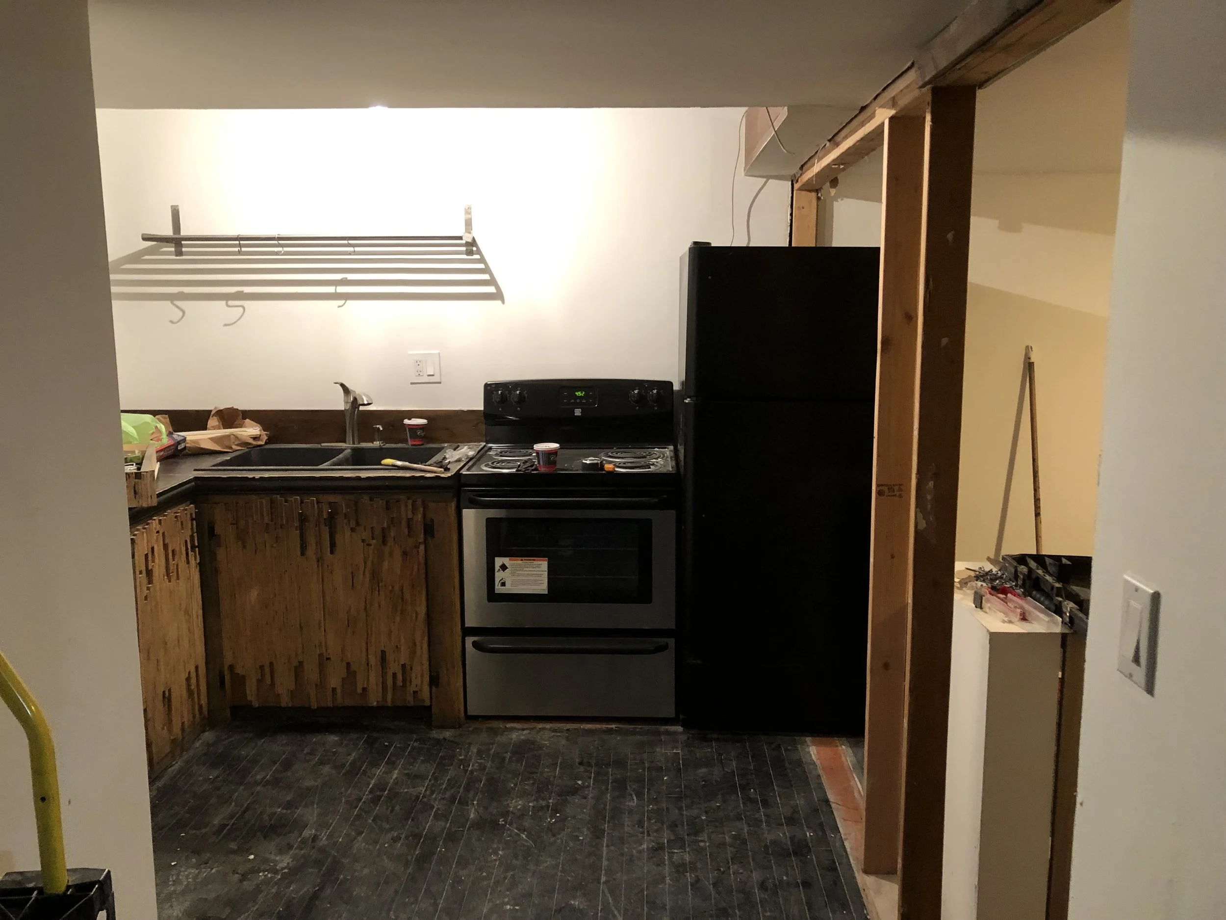 Kitchen under renovation with wooden cabinets, a black refrigerator, a stove, and construction tools on the counter.
