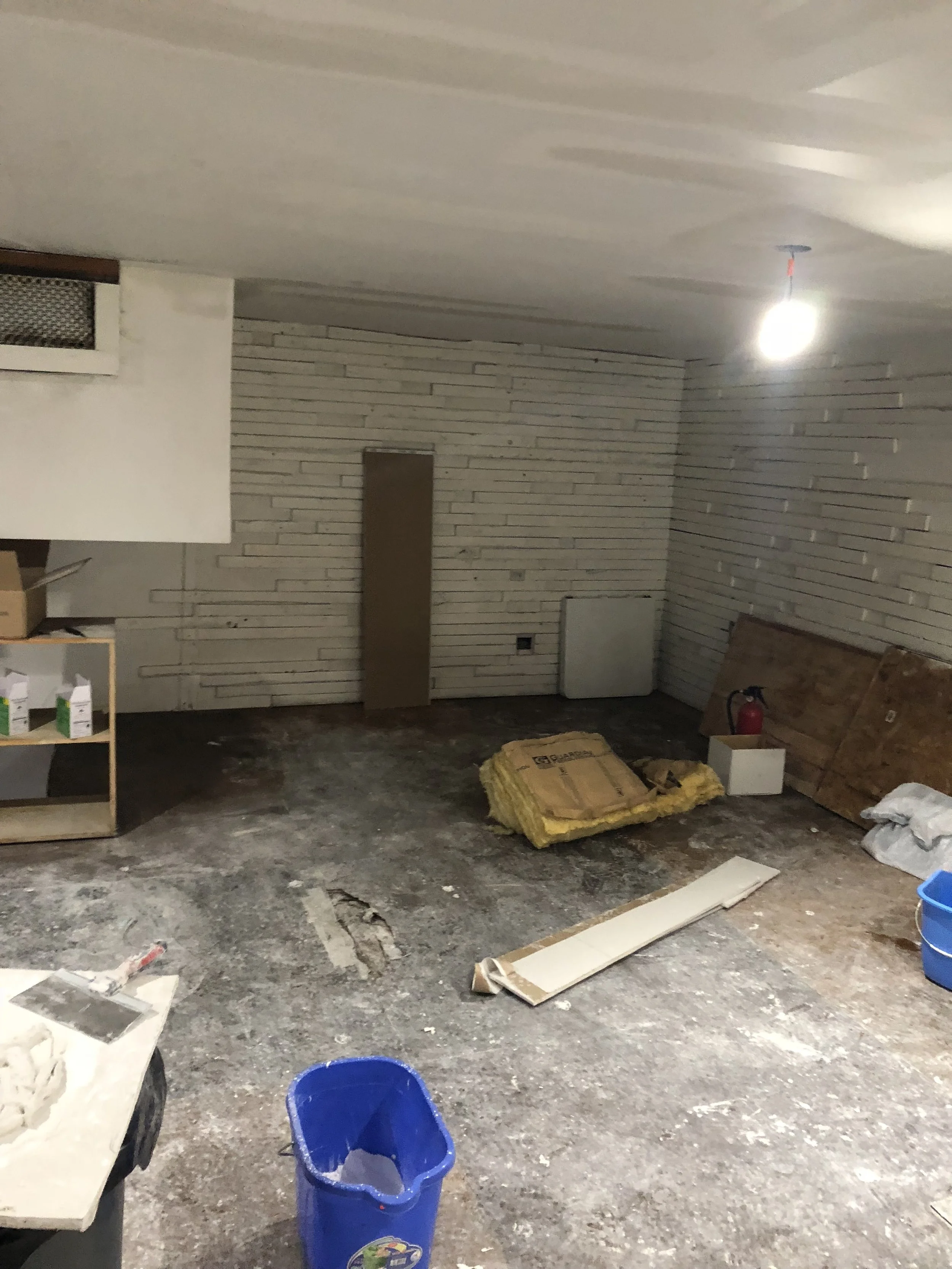 Unfinished basement with construction materials, including insulation, cardboard boxes, and a fire extinguisher, on a concrete floor.
