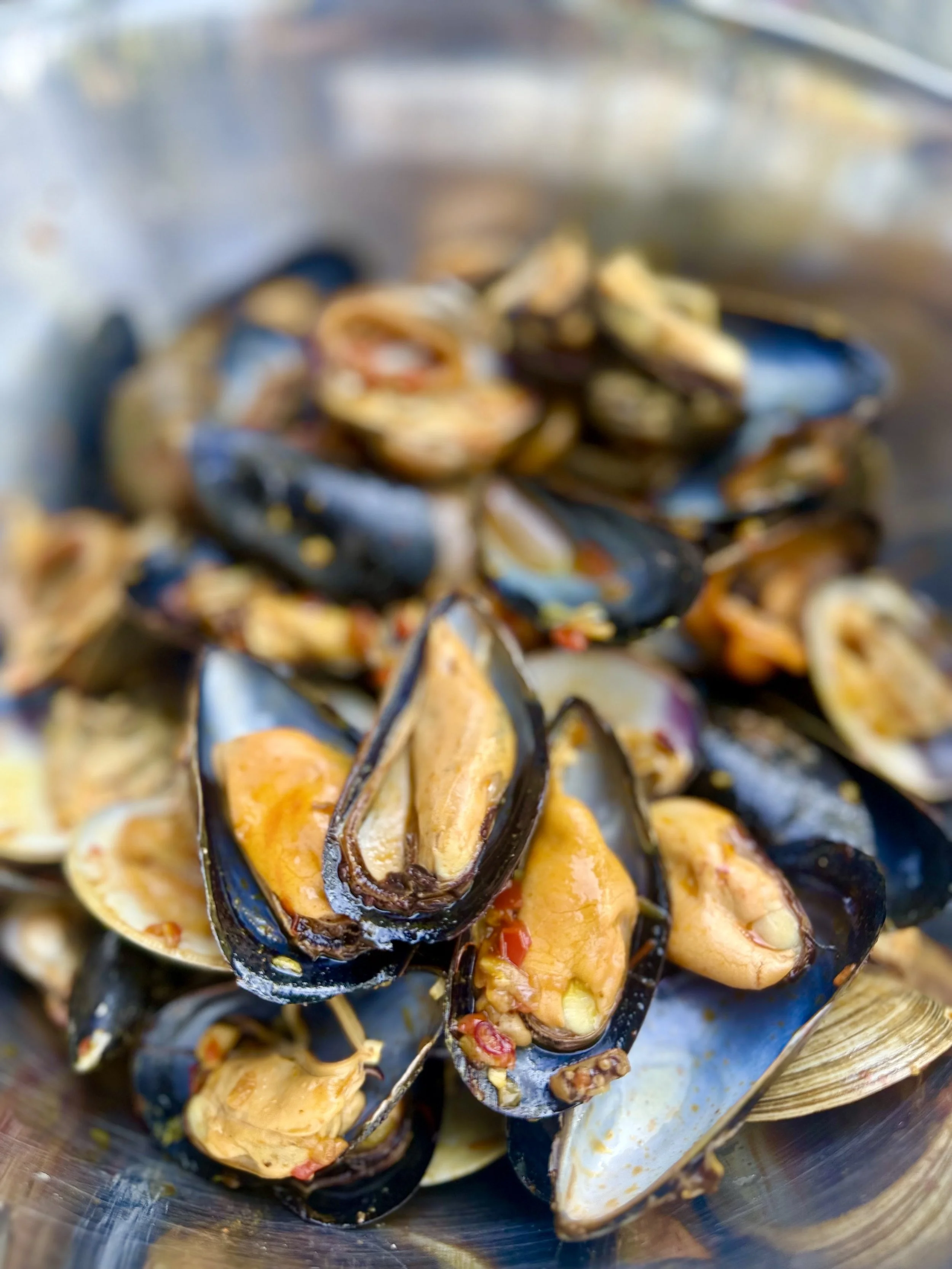 Close-up of cooked mussels with orange and yellow filling in a metal bowl