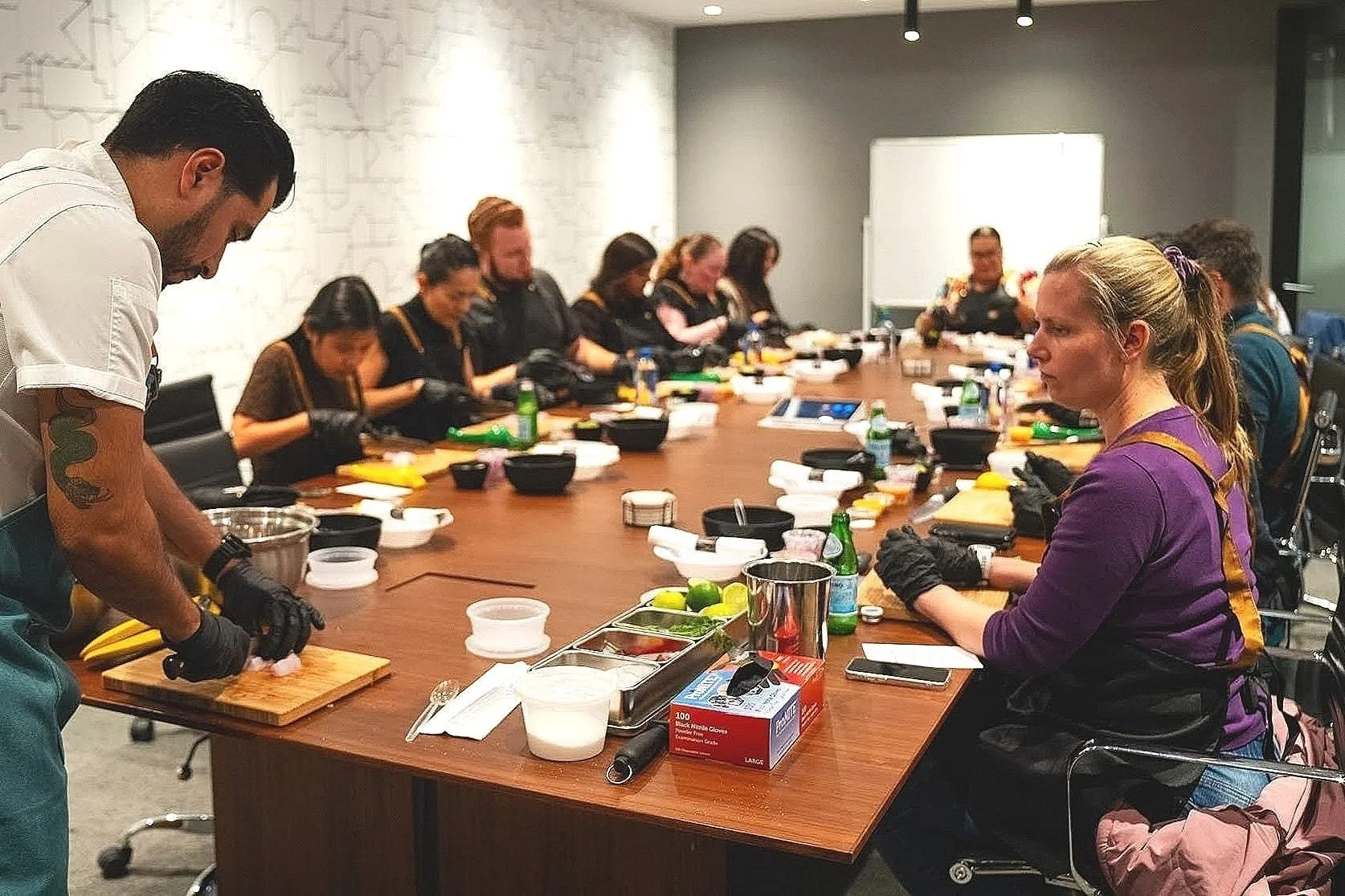 Group of people participating in a cooking class in a conference room, with ingredients and kitchen tools on the table.