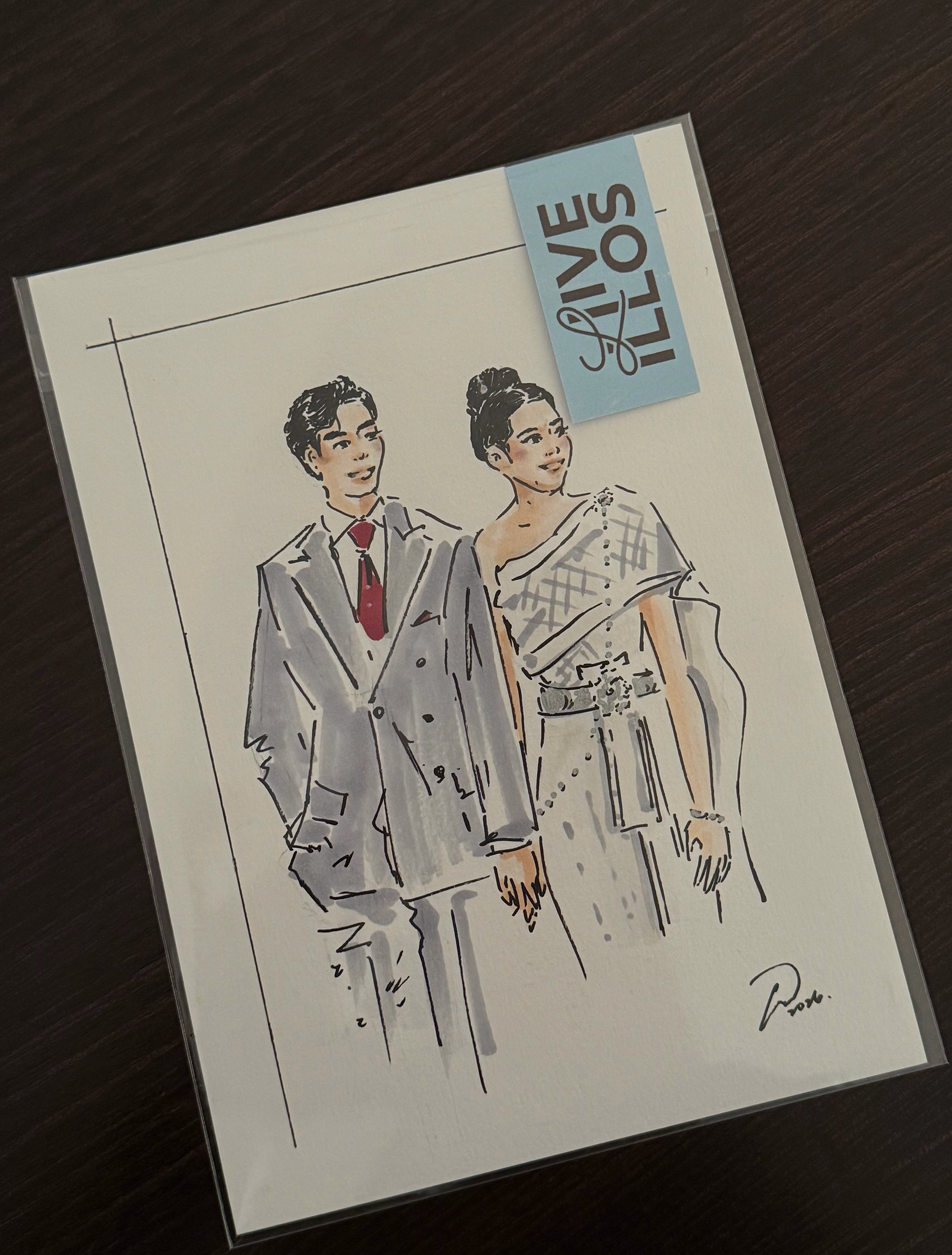 A coloring illustration of a man and woman dressed in formal attire, with the woman wearing traditional thai dress and the man in a suit, posed together on a piece of paper