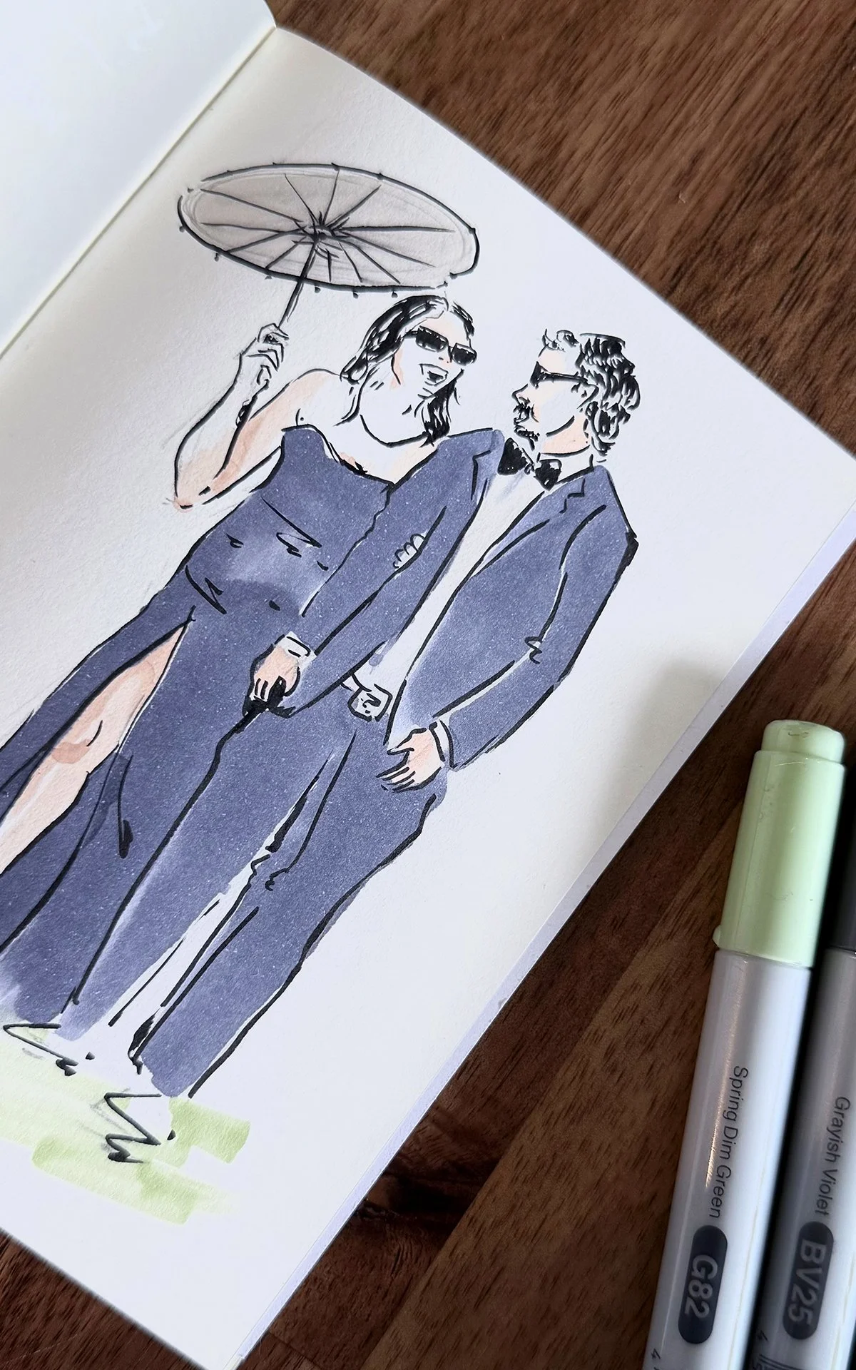 A watercolor illustration of a stylish woman in a slitted gown holding an umbrella and a man in a tuxedo with glasses, with a wooden surface and some markers nearby.